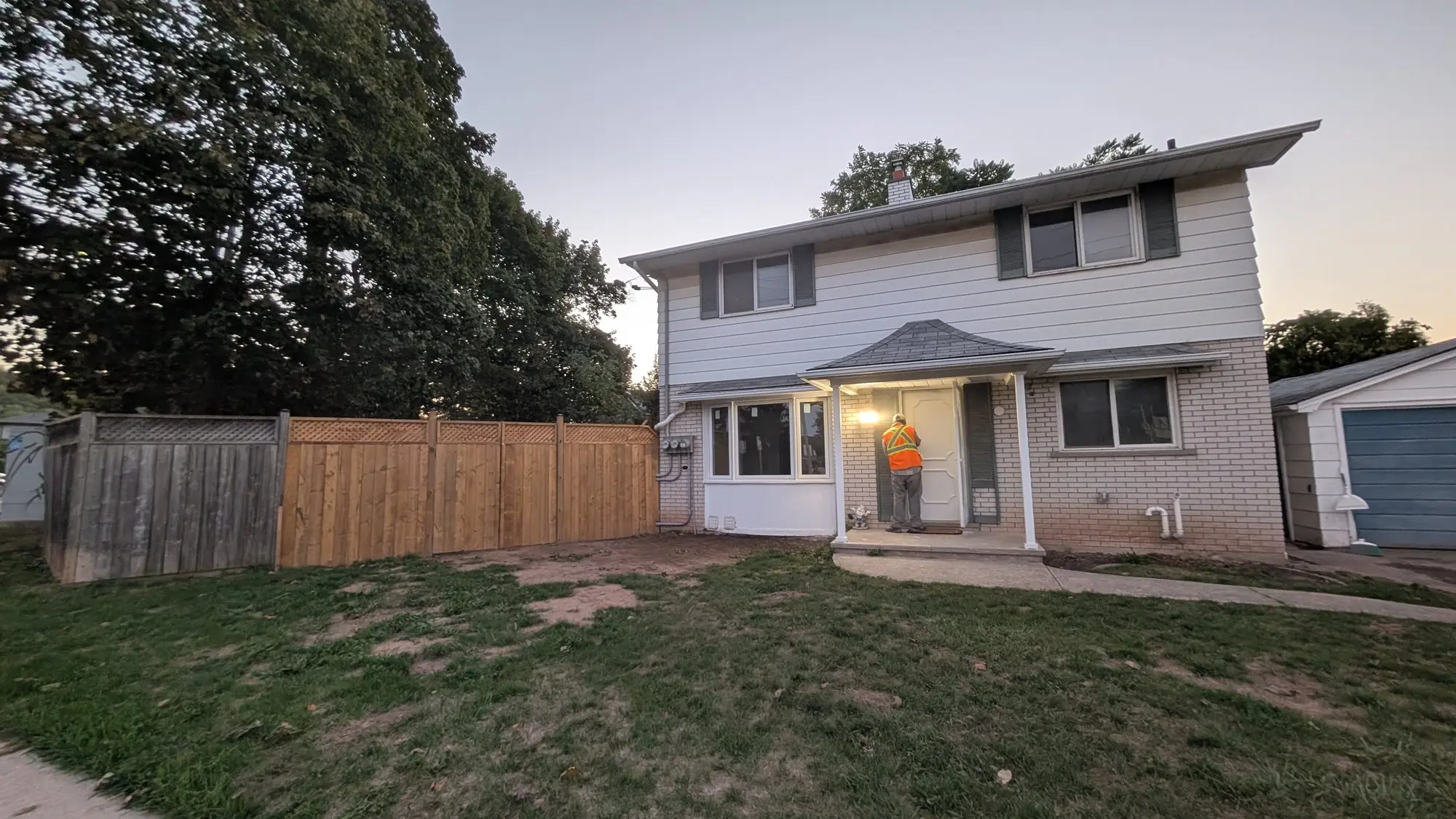 The finished two-storey home from the street at dusk, with new siding and a lit front entrance