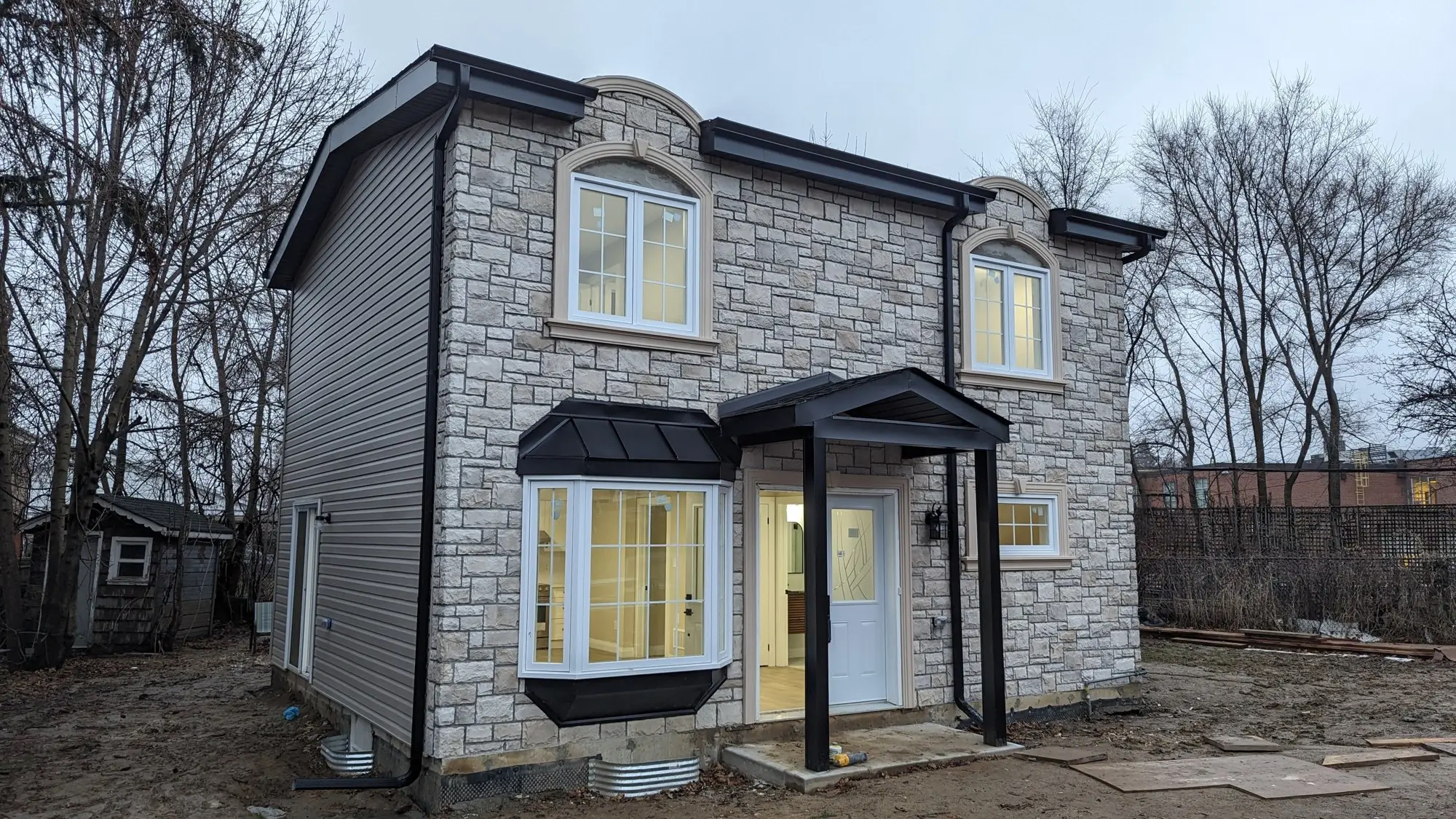 The completed two-storey garden suite from the front, with stone facade, gabled entry canopy and bay window