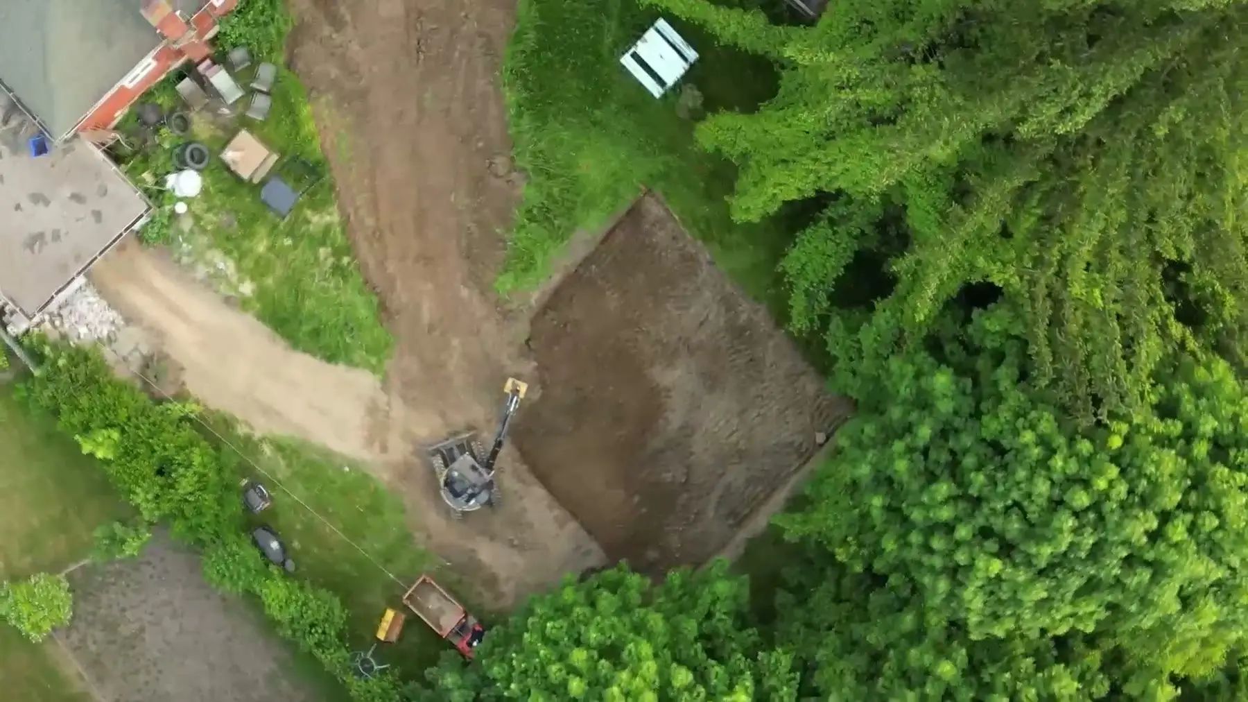 Aerial view of the rear yard excavation, with the mature trees and the existing house at the front of the lot