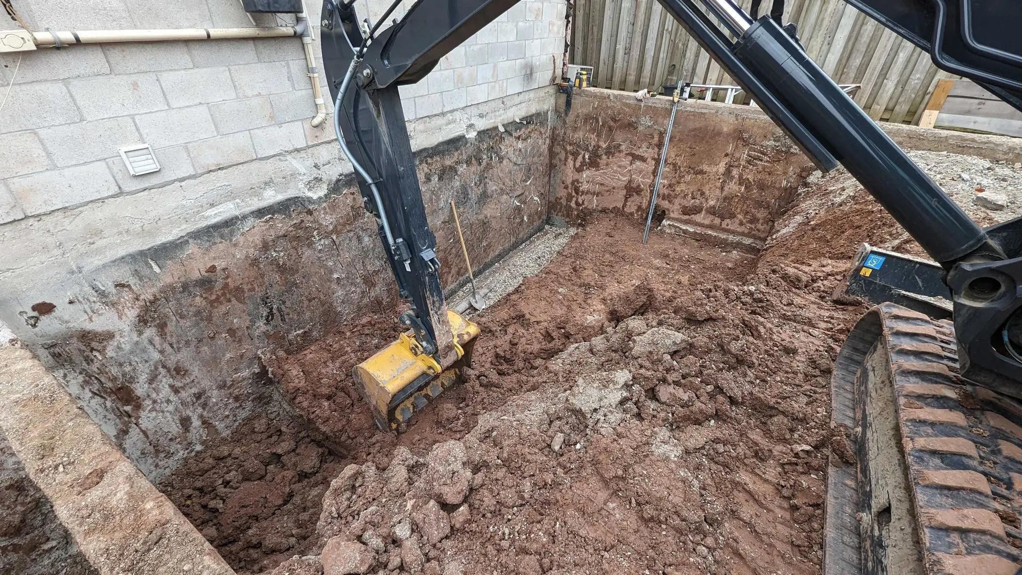 Excavator cutting the foundation trench alongside the existing house