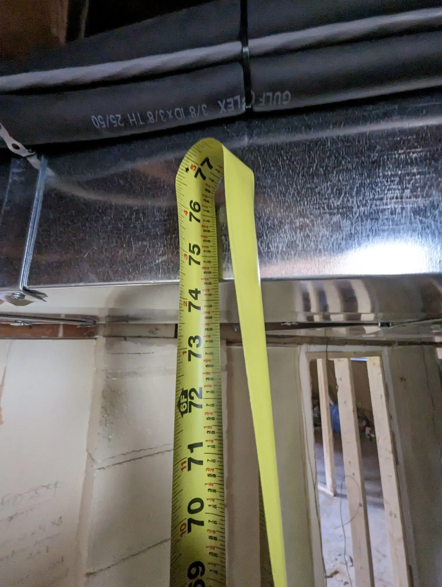 Tape measure held to the underside of the basement joists showing the original ceiling clearance