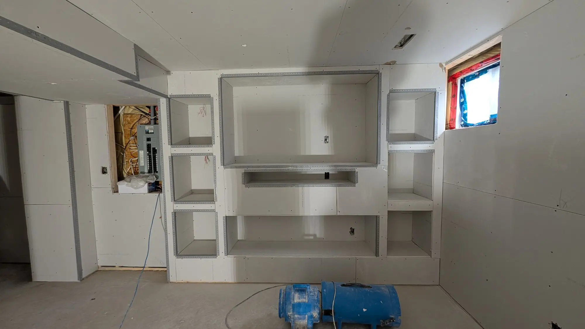 The media wall framed and boarded with recessed shelving and fireplace opening