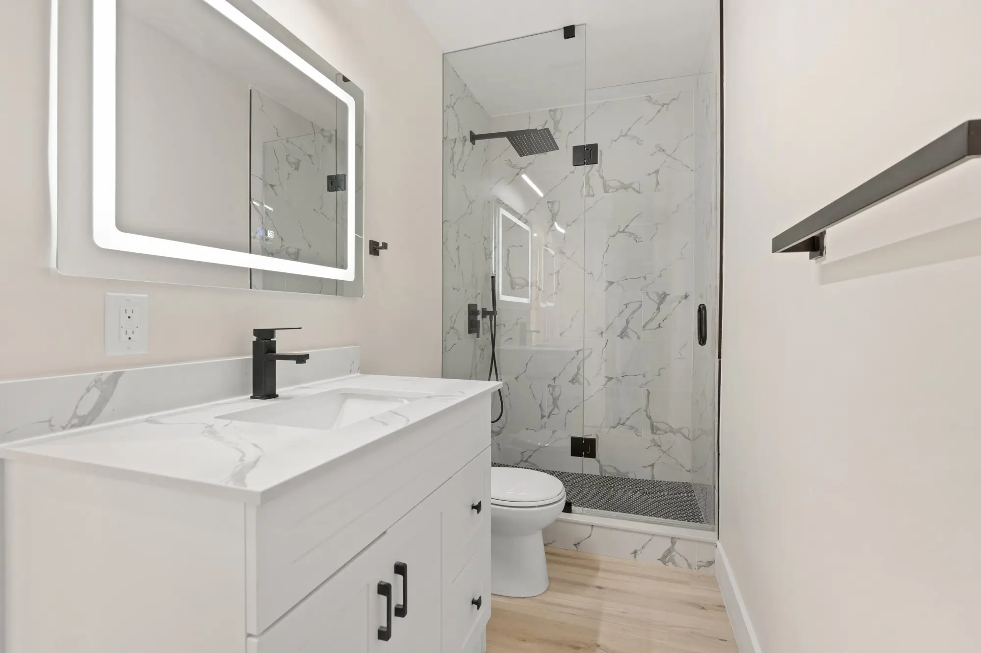 Completed bathroom with marble-look tile, glass shower and LED mirror