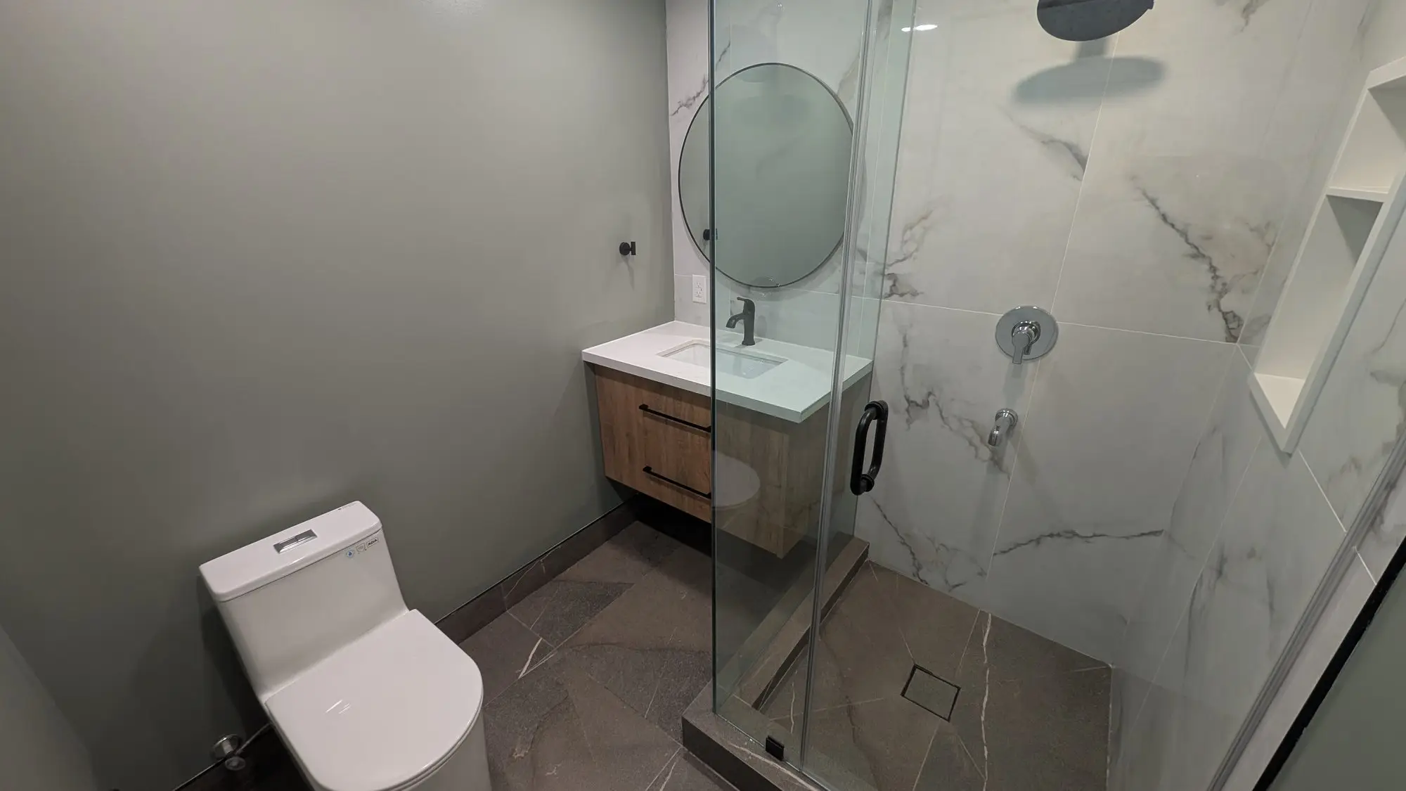 Floating walnut vanity with round mirror and matte black fixtures
