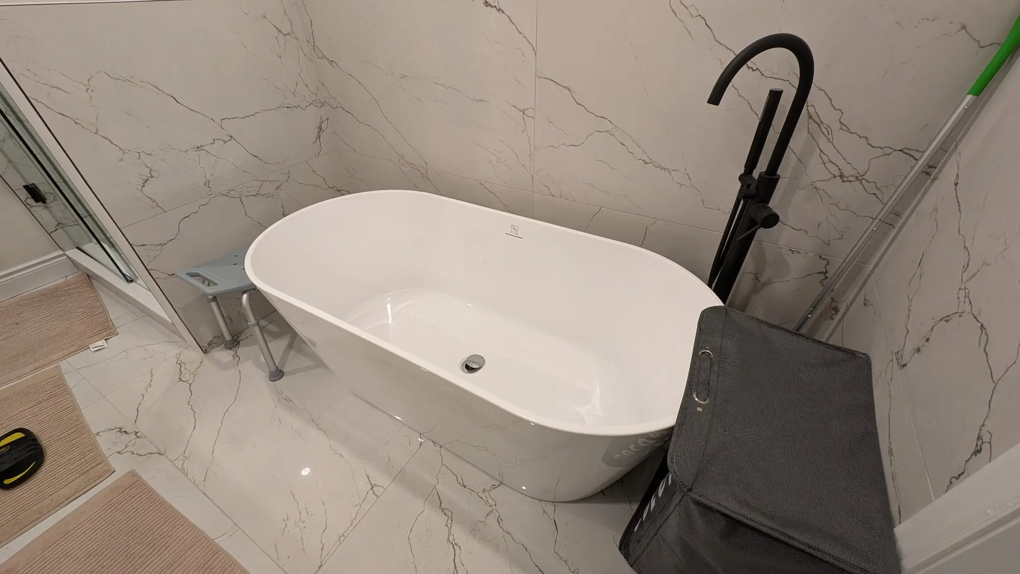 Freestanding tub with floor-mounted black filler against marble-look porcelain