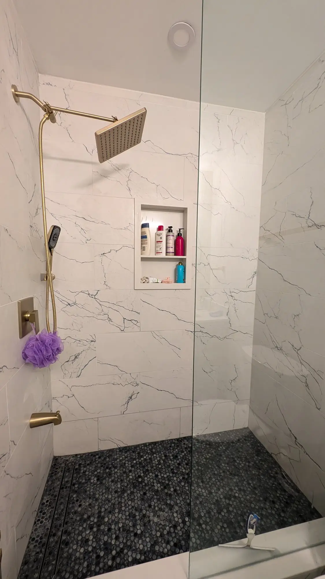 Walk-in shower with pebble floor, recessed niche and gold fixtures