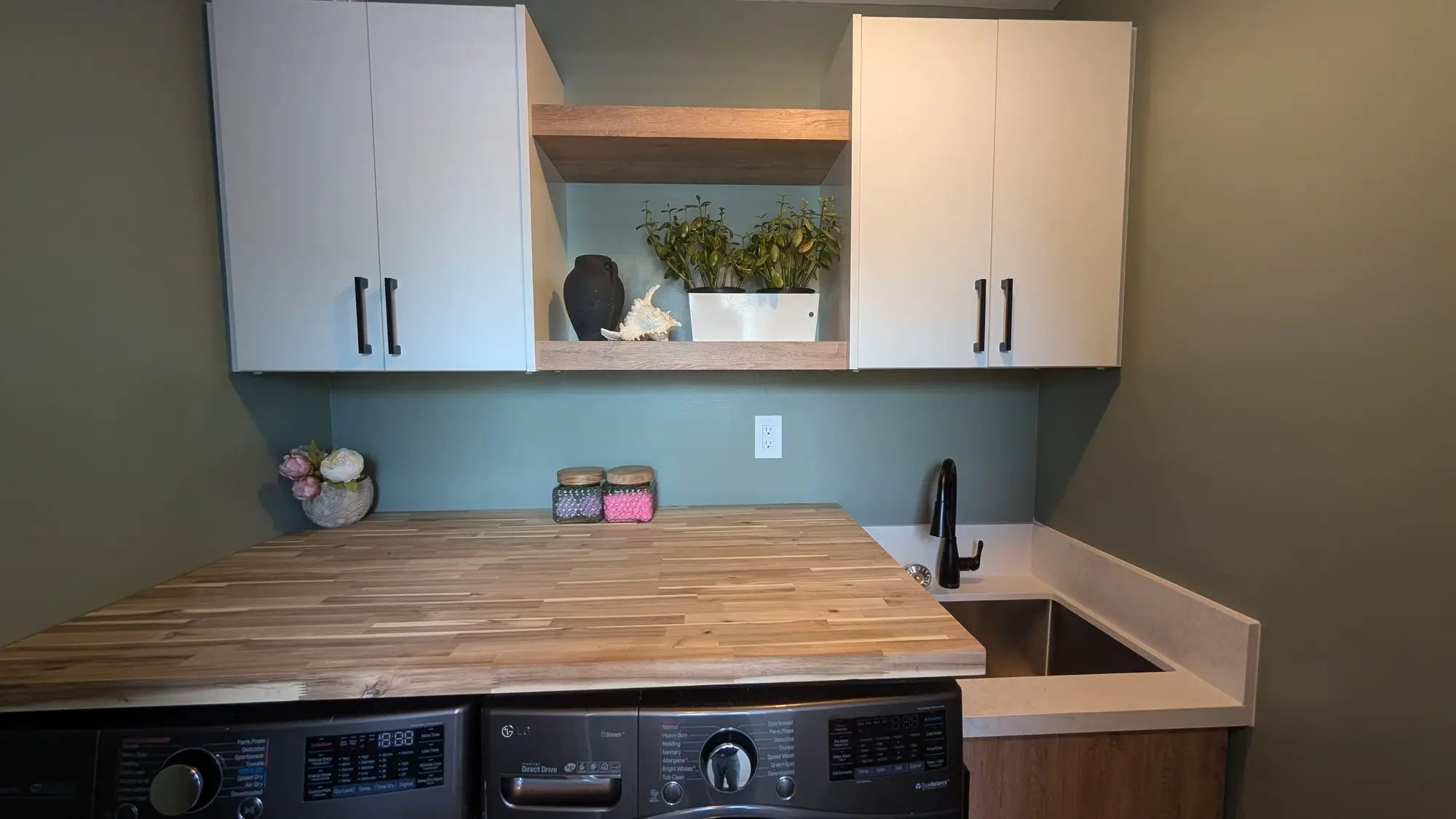 Laundry counter, sink and open shelving against sage green walls