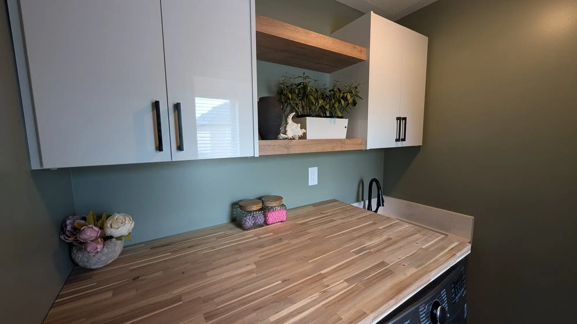 Two-tone laundry cabinetry with open shelf and butcher-block surface