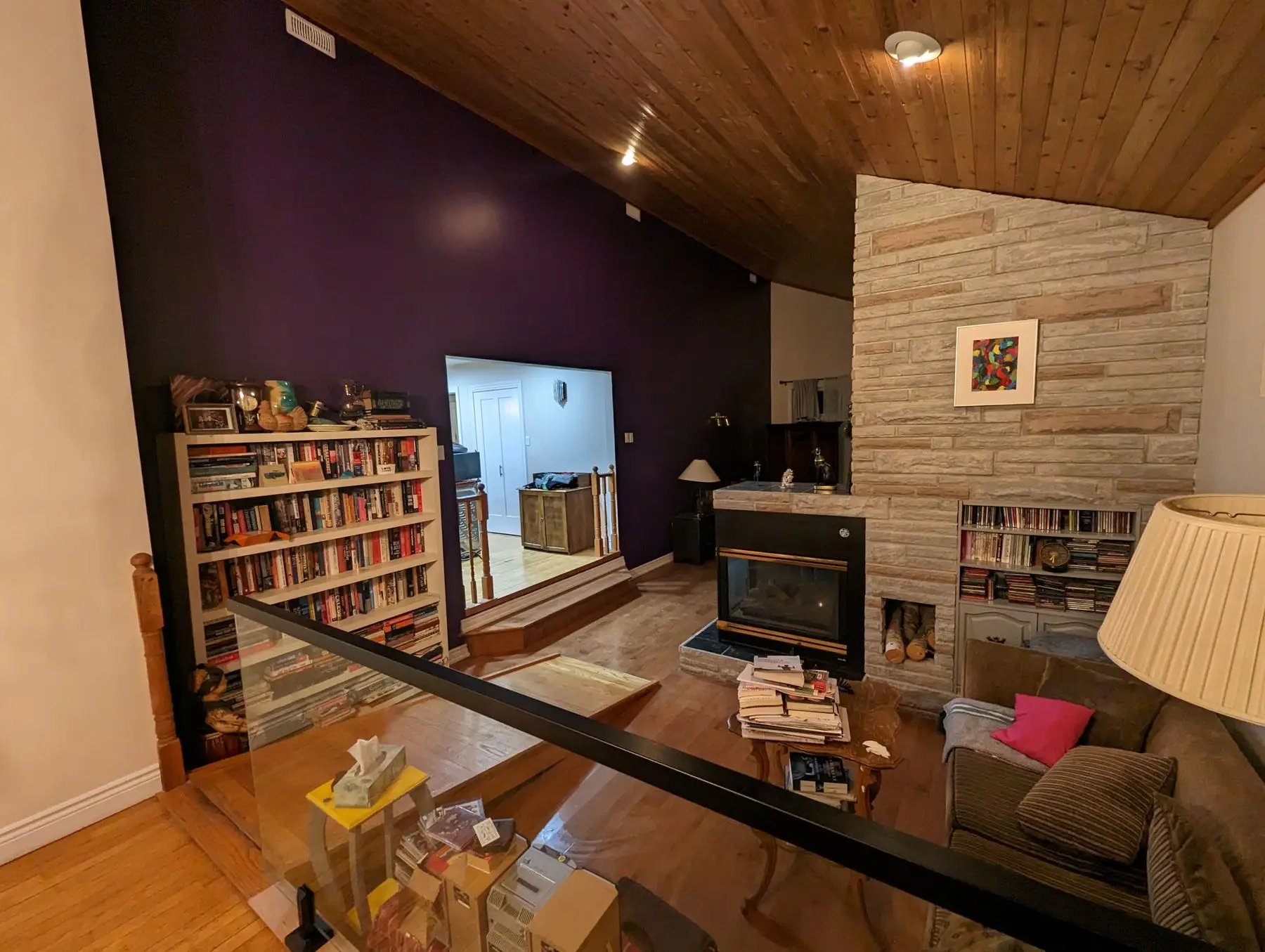 Before — Spacious living room with stone fireplace, wood-slat vaulted ceiling, and purple accent wall.