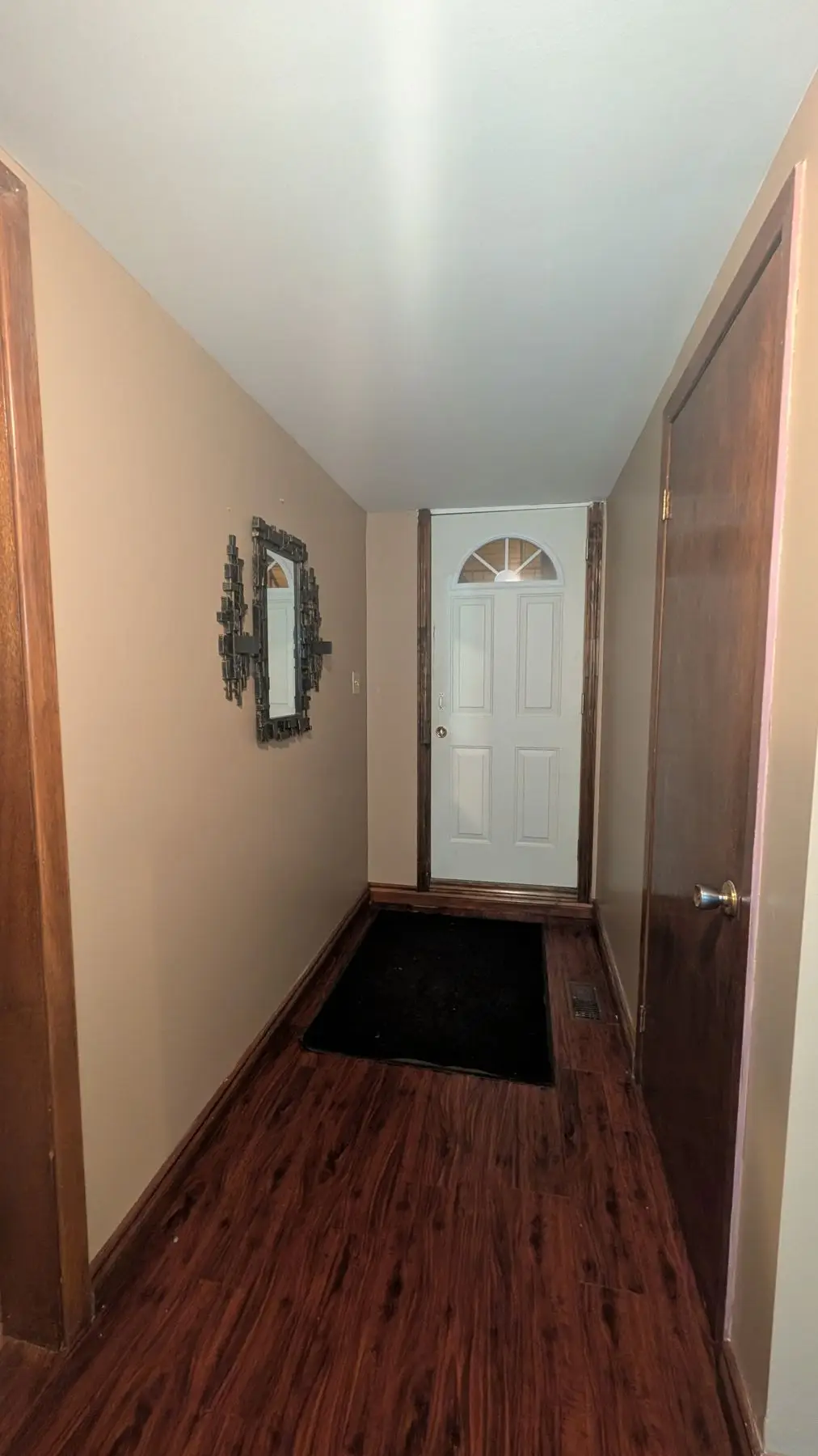 Before — Wide shot of a hallway entrance before renovation with dark wood flooring and tan walls.