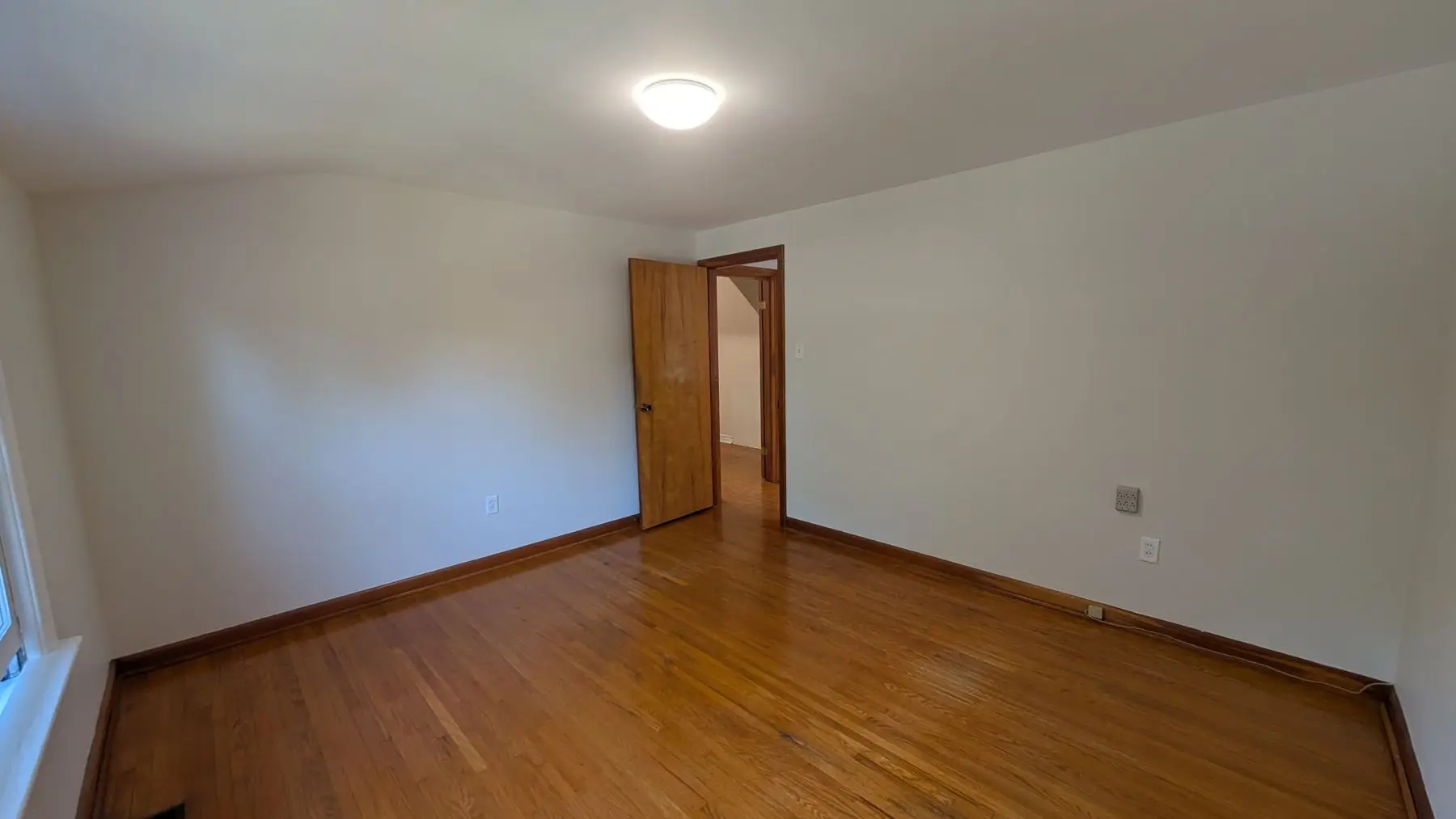 Before — Empty bedroom with hardwood floors, white walls, and a wooden door.