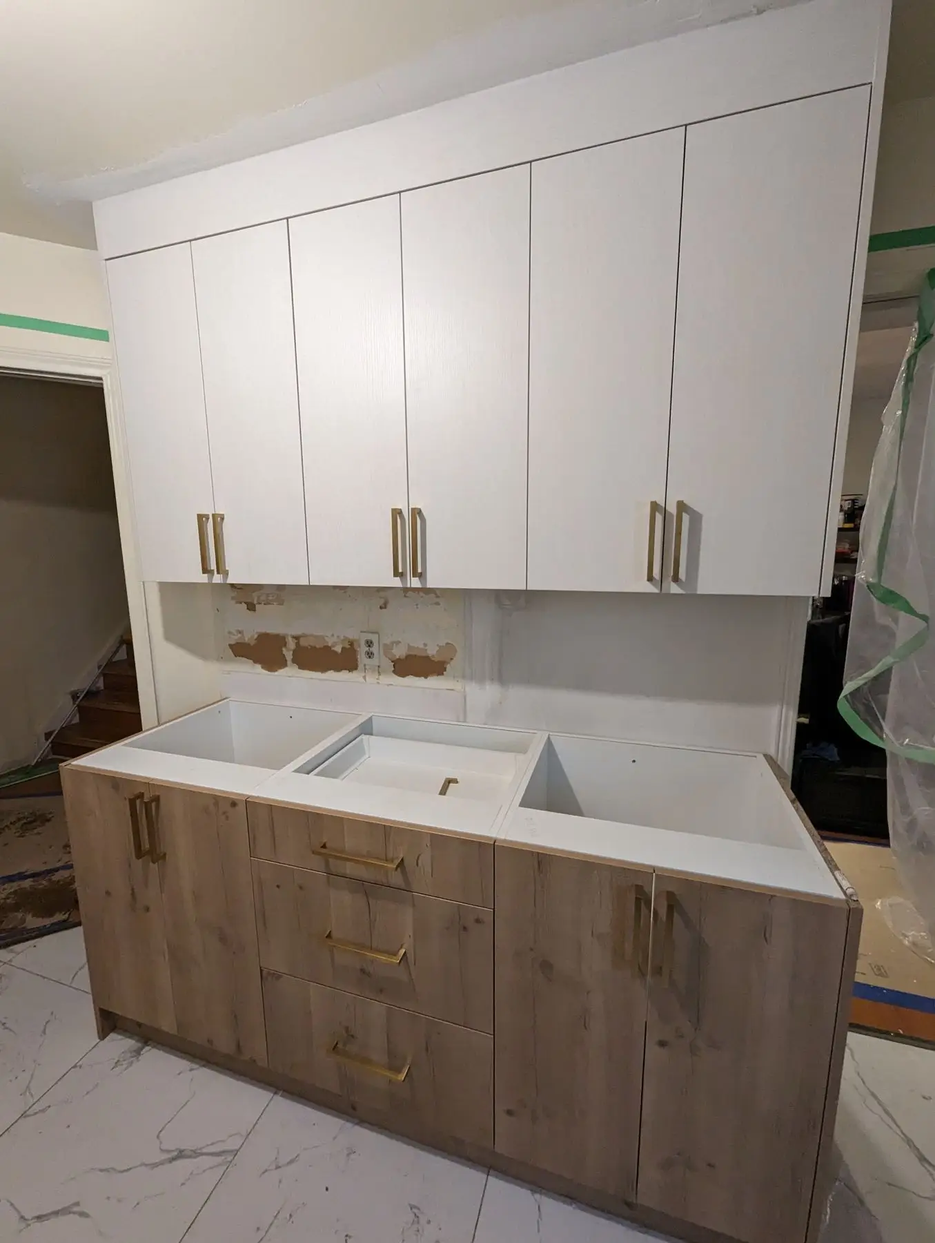 Finishing — Laundry room cabinetry installation in progress with unfinished backsplash area and protective masking.