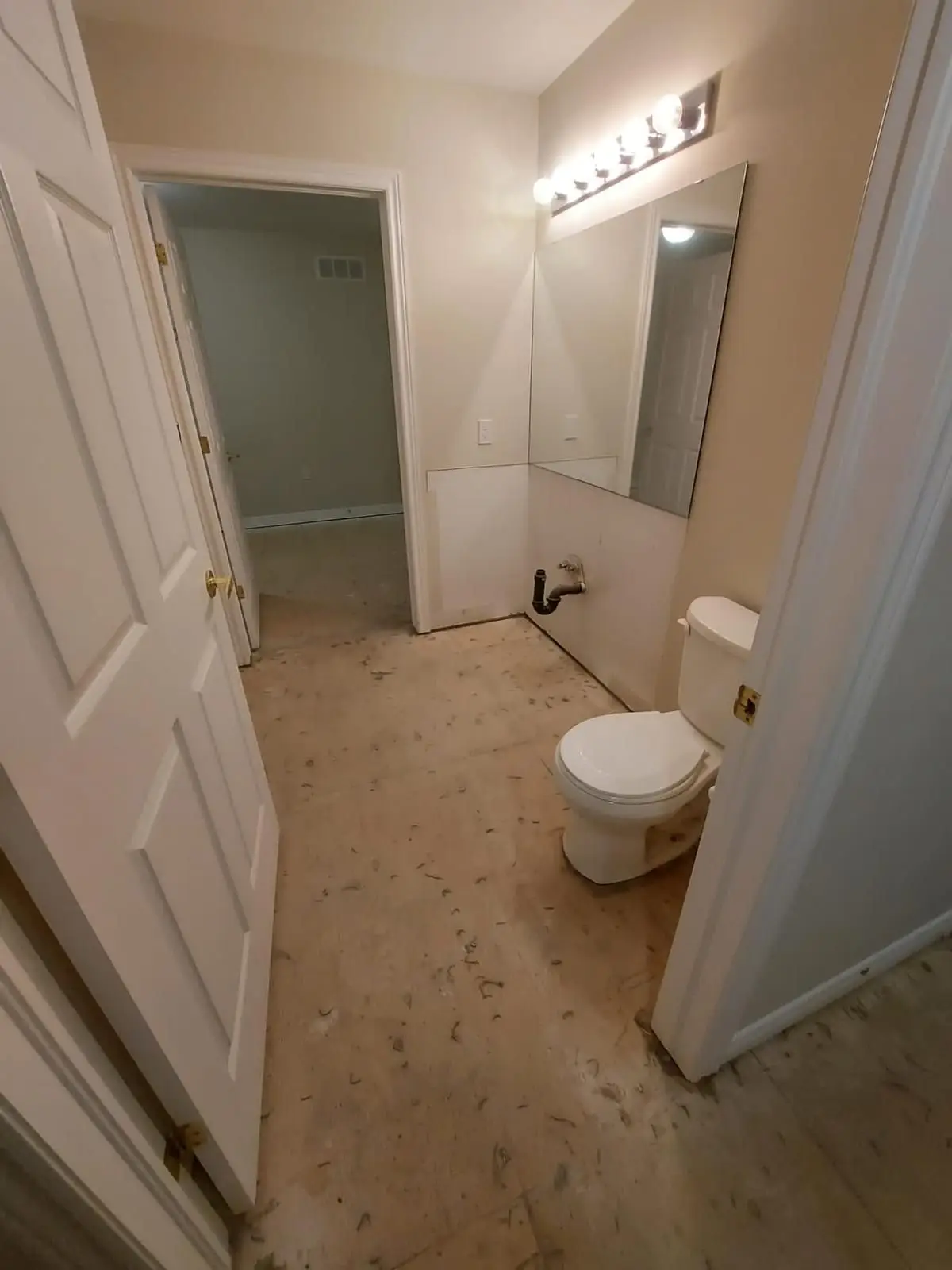 Demolition — Bathroom undergoing demolition with subfloor exposed and vanity removed, showing toilet and mirror.