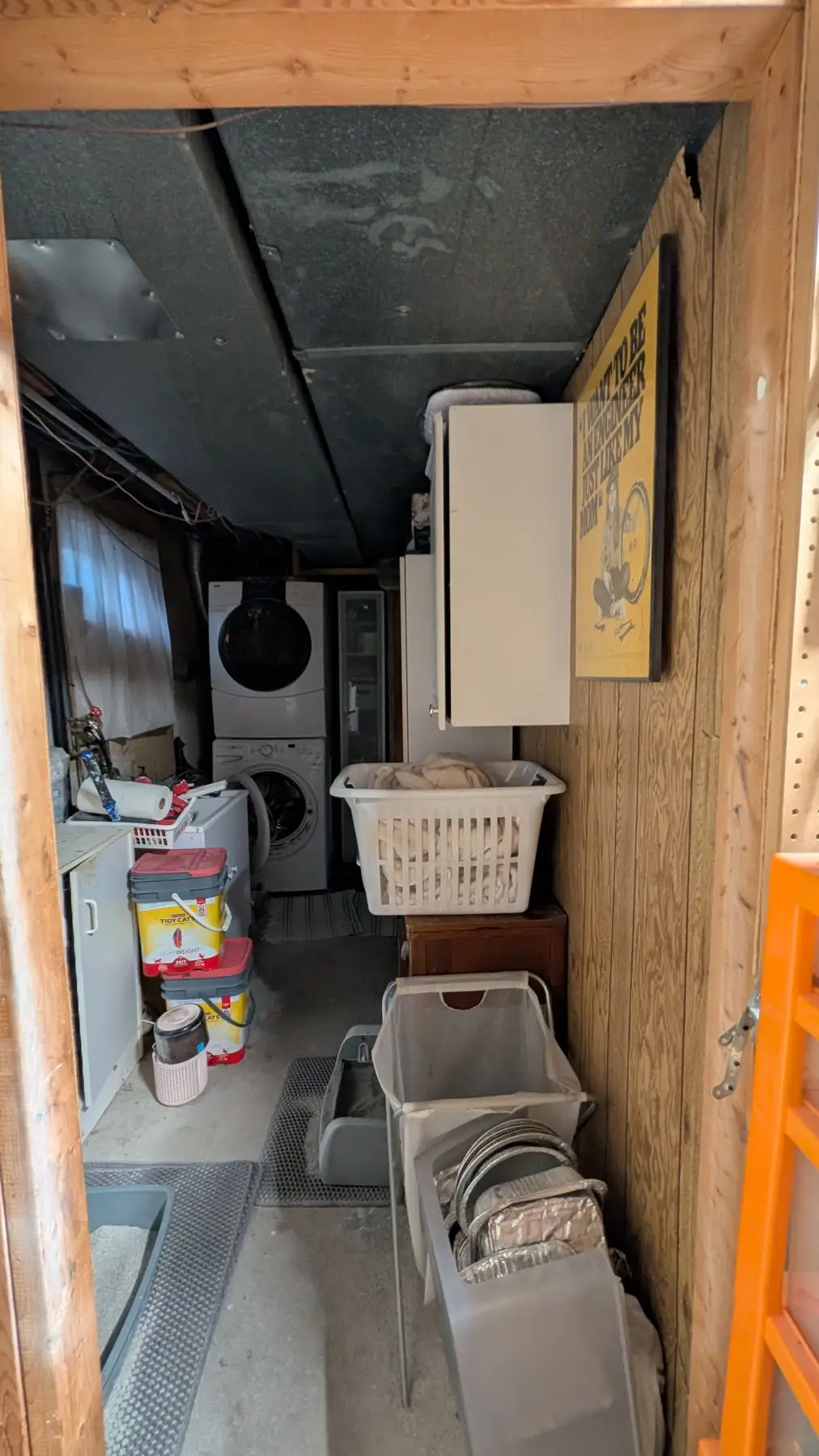 Before — Basement laundry room with stacked washer and dryer viewed from the doorway.