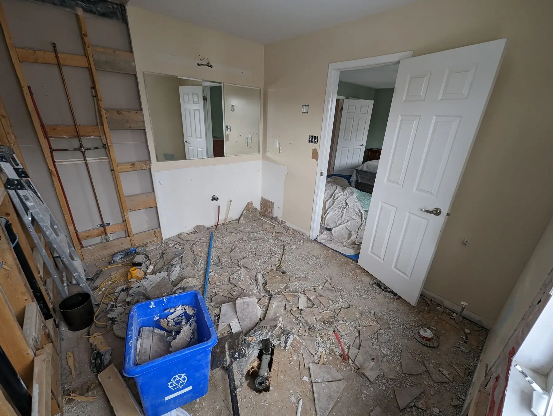 Demolition — Bathroom undergoing tile demolition with debris on the floor and a blue recycling bin.