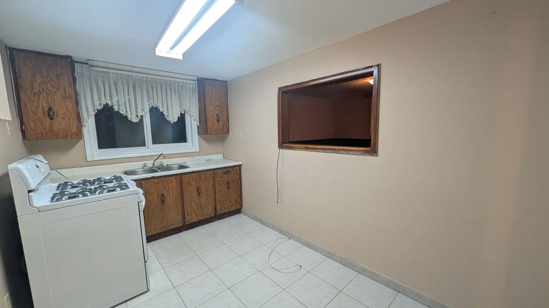 Before — Dated kitchen with wood cabinets, white appliances, and a pass-through wall opening.