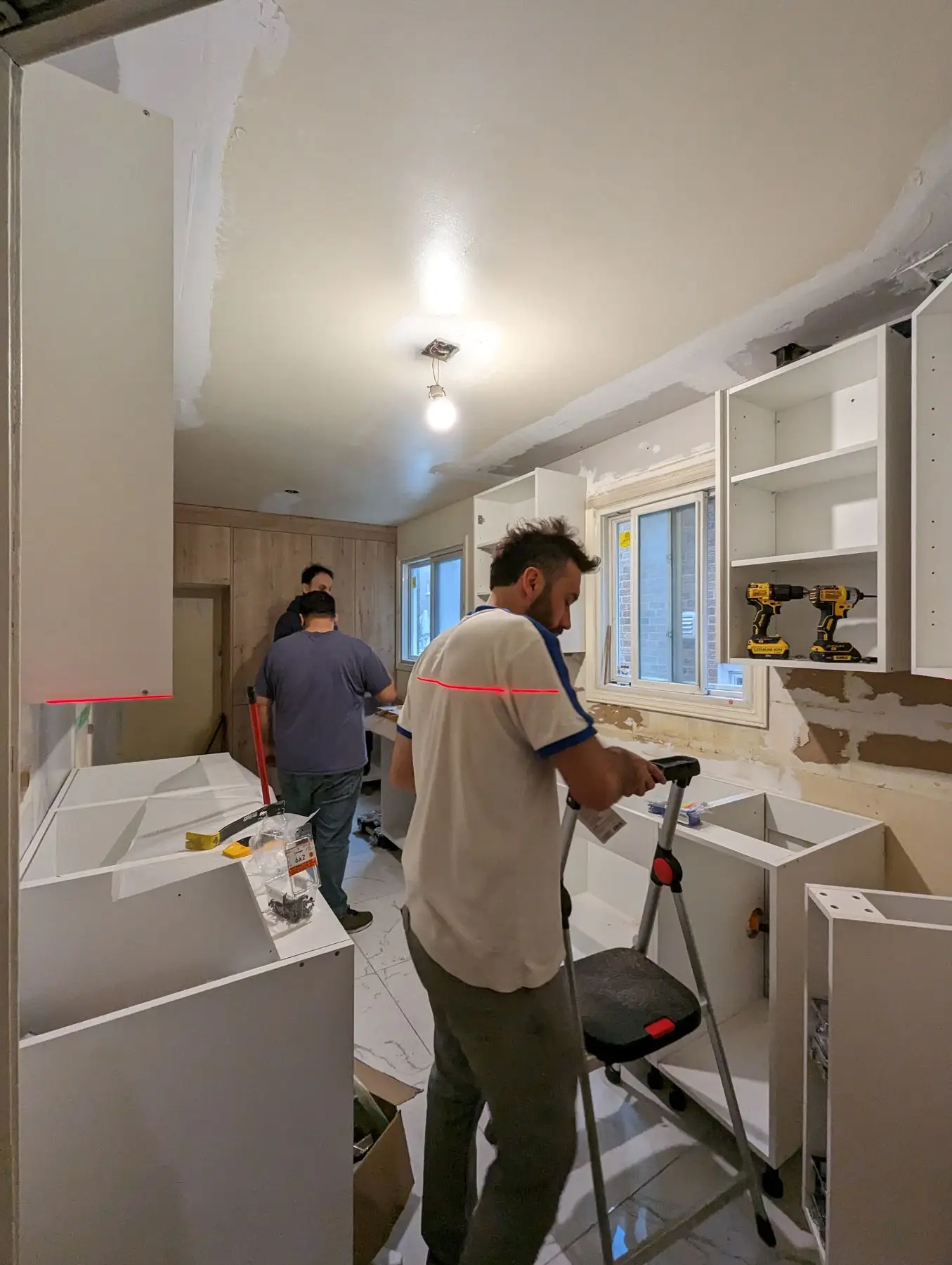 Finishing — Workers installing kitchen cabinets and setting up upper shelving units in a progress stage.