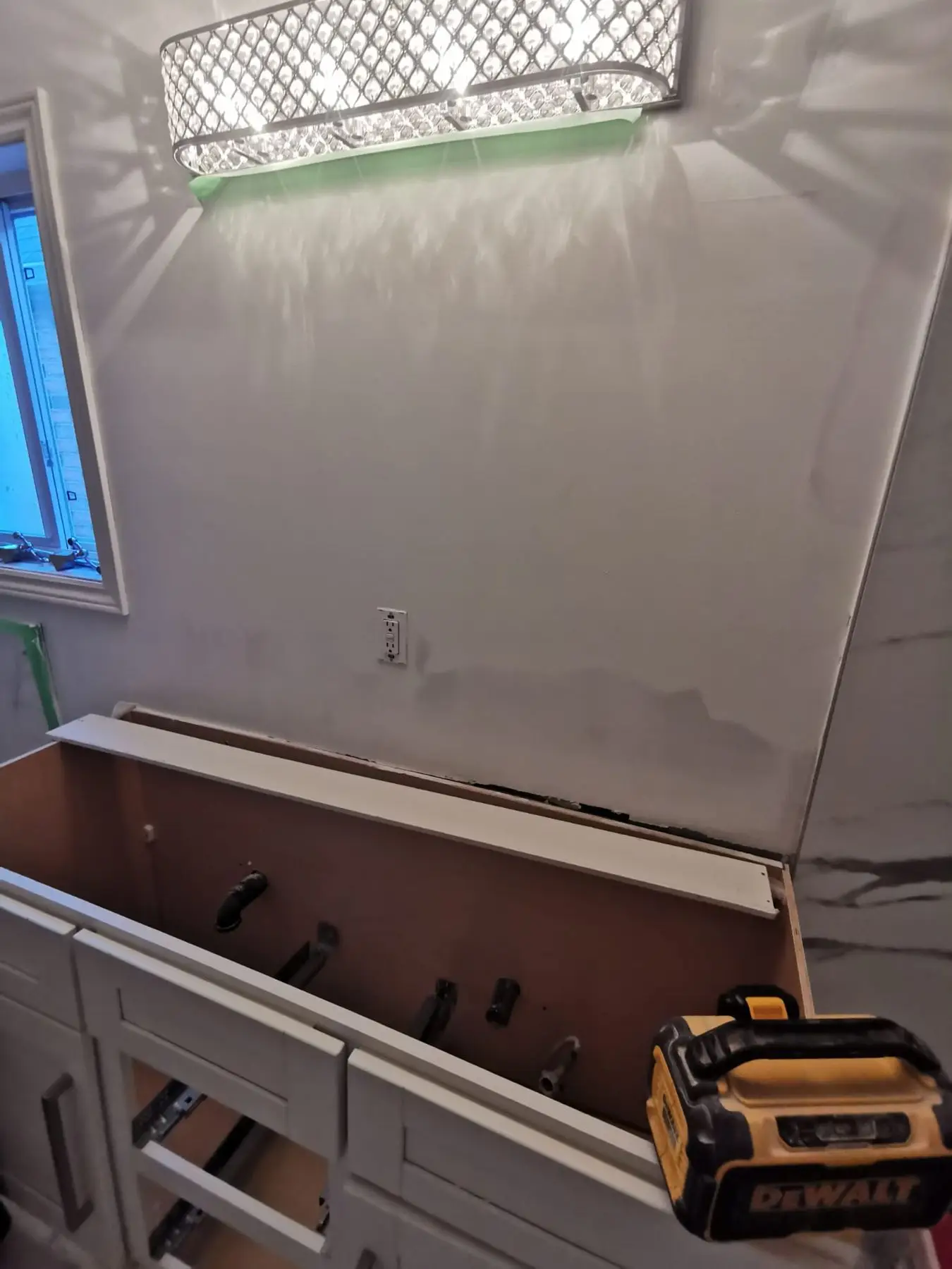 Insulation & drywall — Bathroom vanity base installed under drywall patching phase with a Dewalt radio on top.