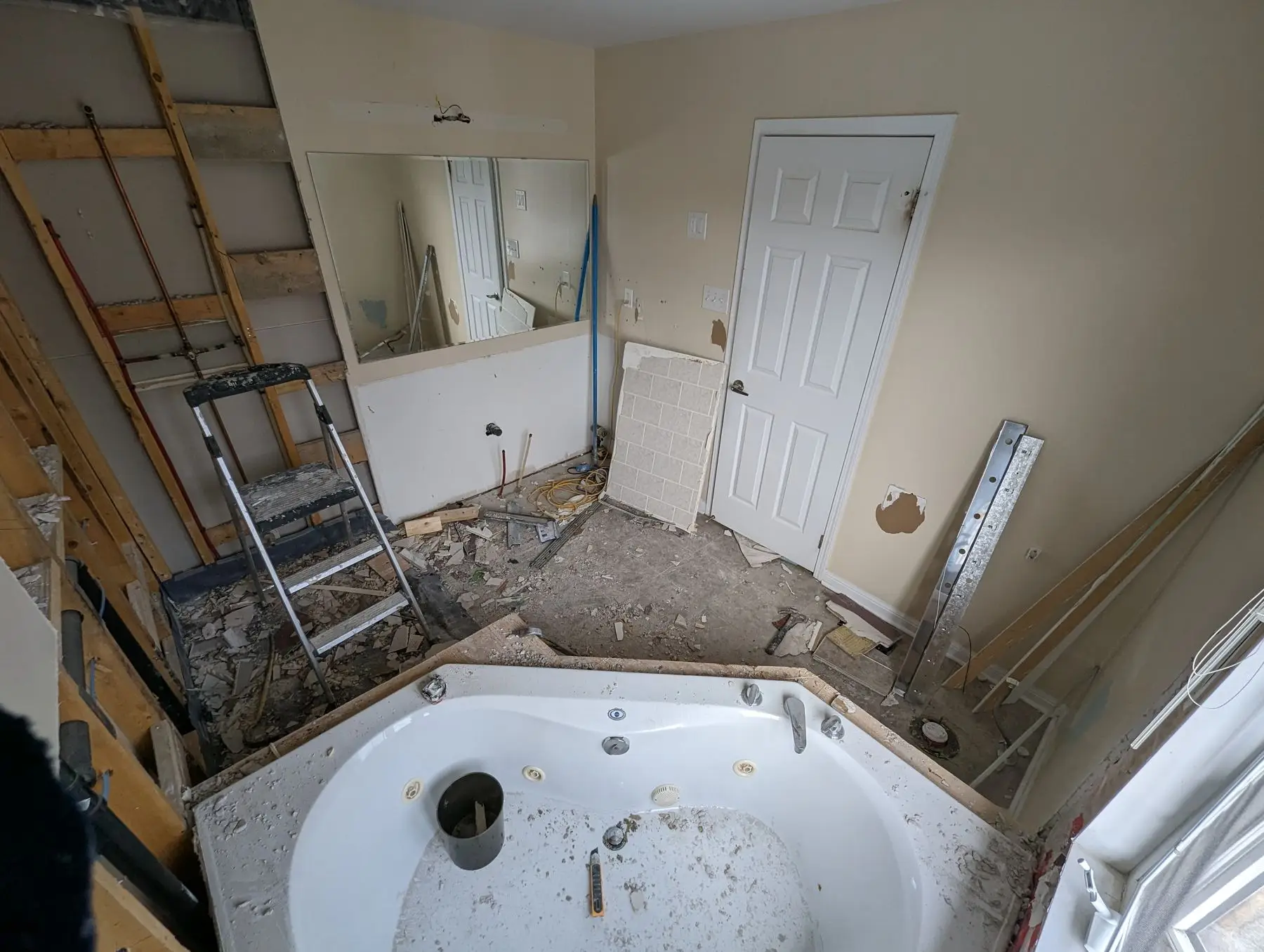 Demolition — Bathroom undergoing demolition with removed drywall, debris on floor, step ladder, and exposed framing.