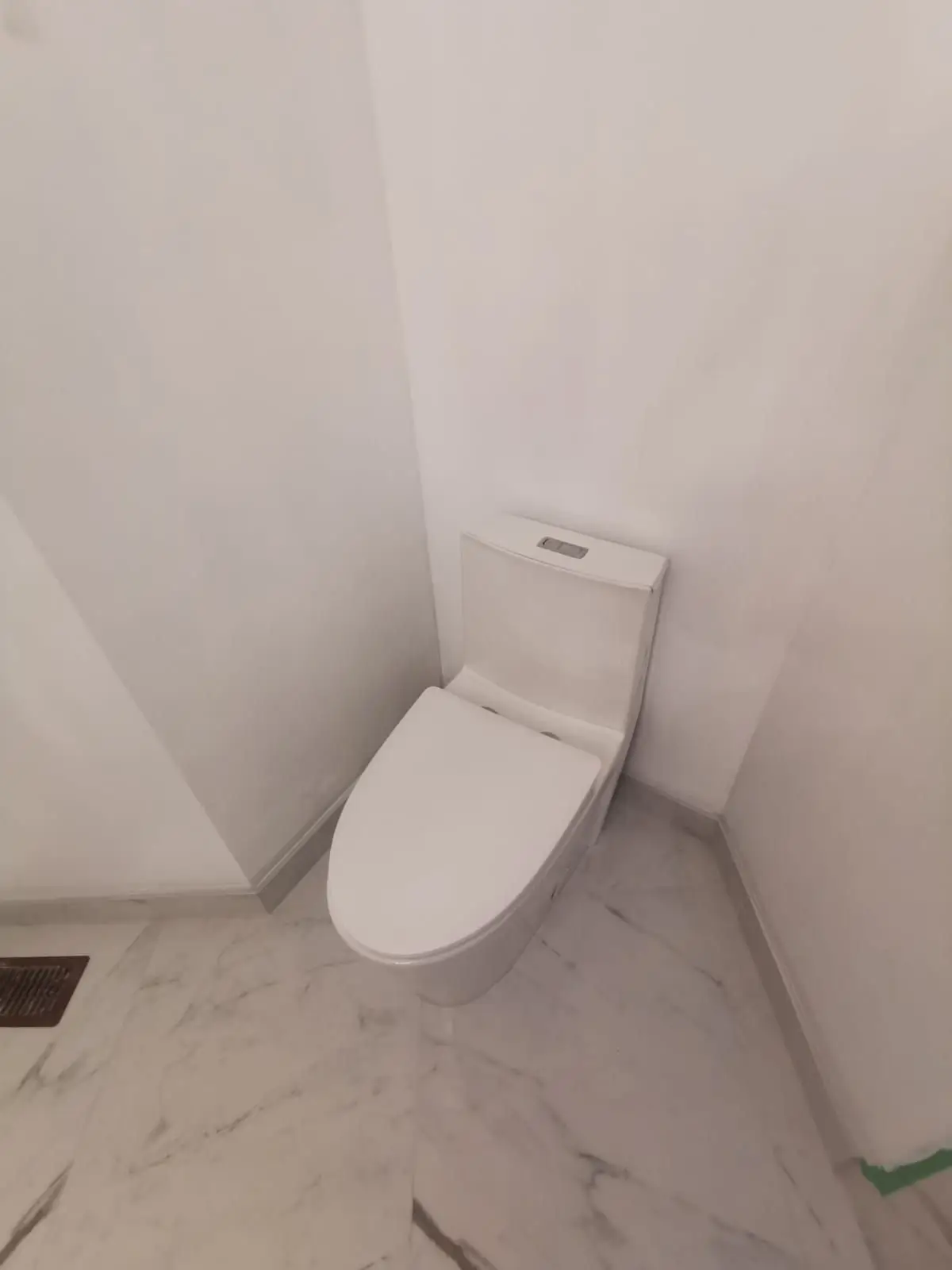 Finishing — A newly installed white modern toilet in the corner of a bathroom with marble-look floor tiles.