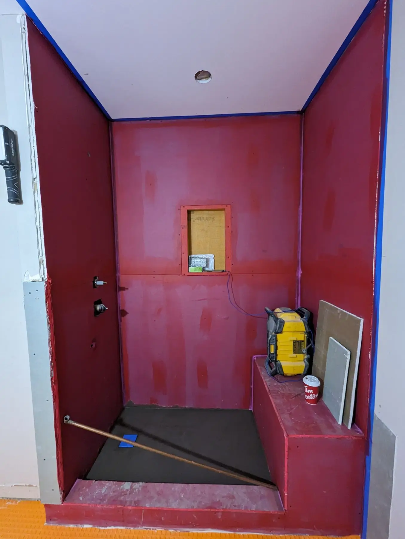 Rough-in — Shower stall waterproofed with red membrane, featuring a built-in niche and bench.