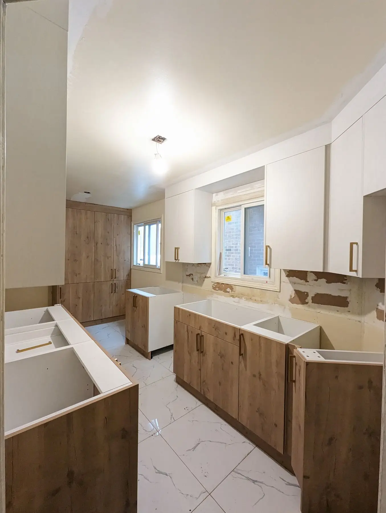 Finishing — Kitchen installation in progress with wooden lower cabinets, white upper cabinets, and tiled flooring.