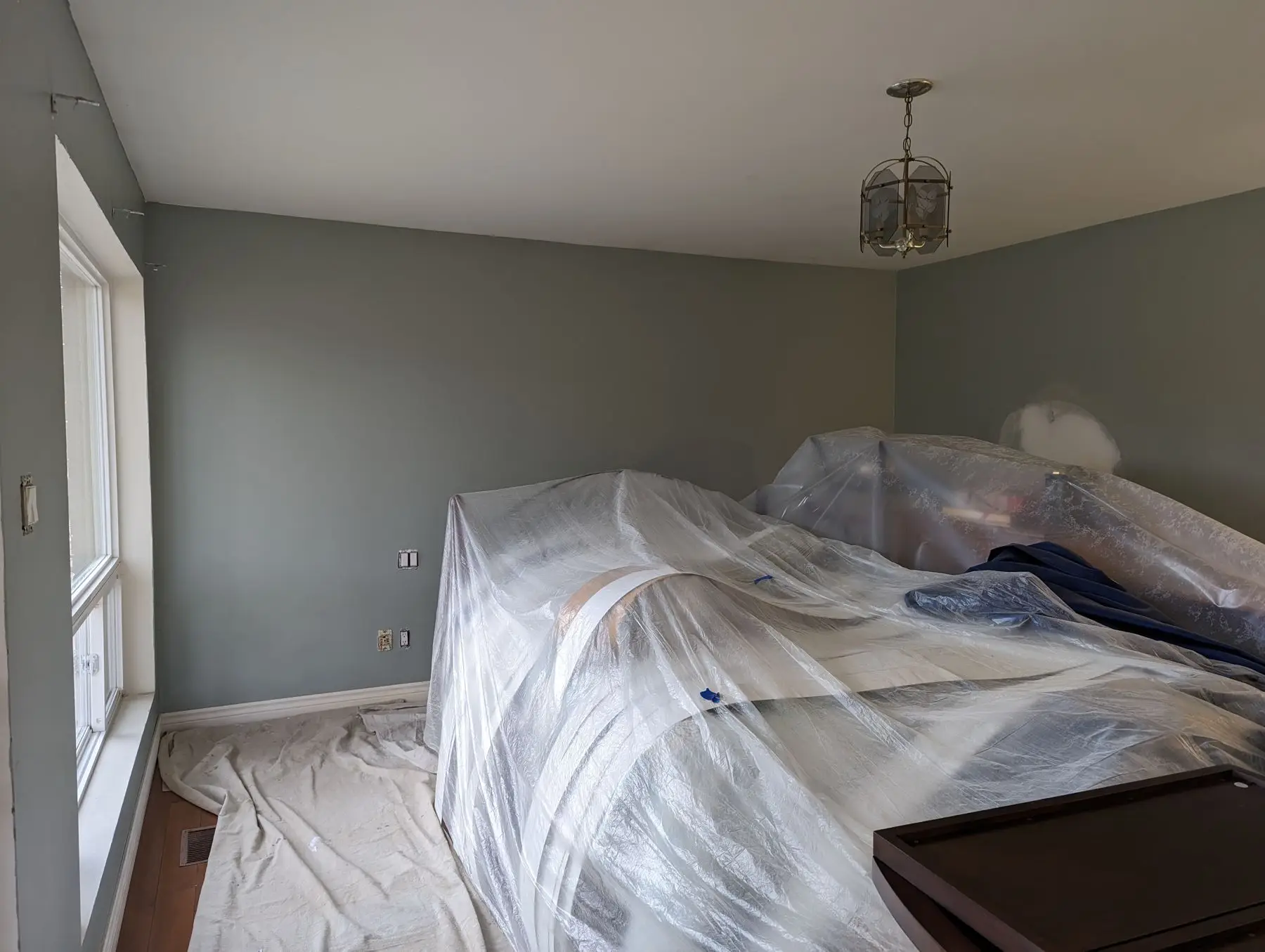 Insulation & drywall — Bedroom under construction with plastic dust covers over furniture and walls painted green.
