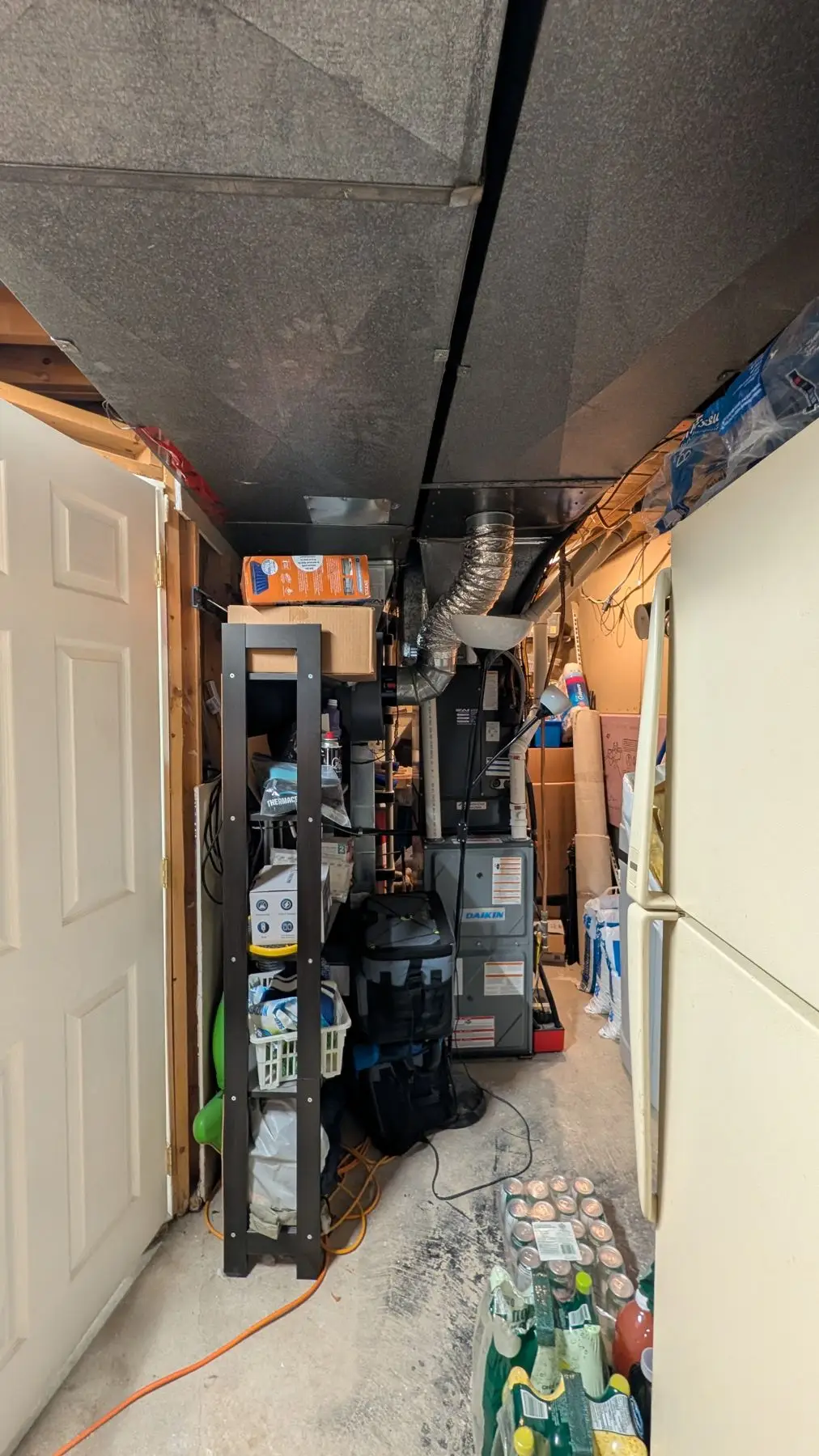 Rough-in — Cluttered mechanical room in a basement showing furnace, ductwork, and stored materials.