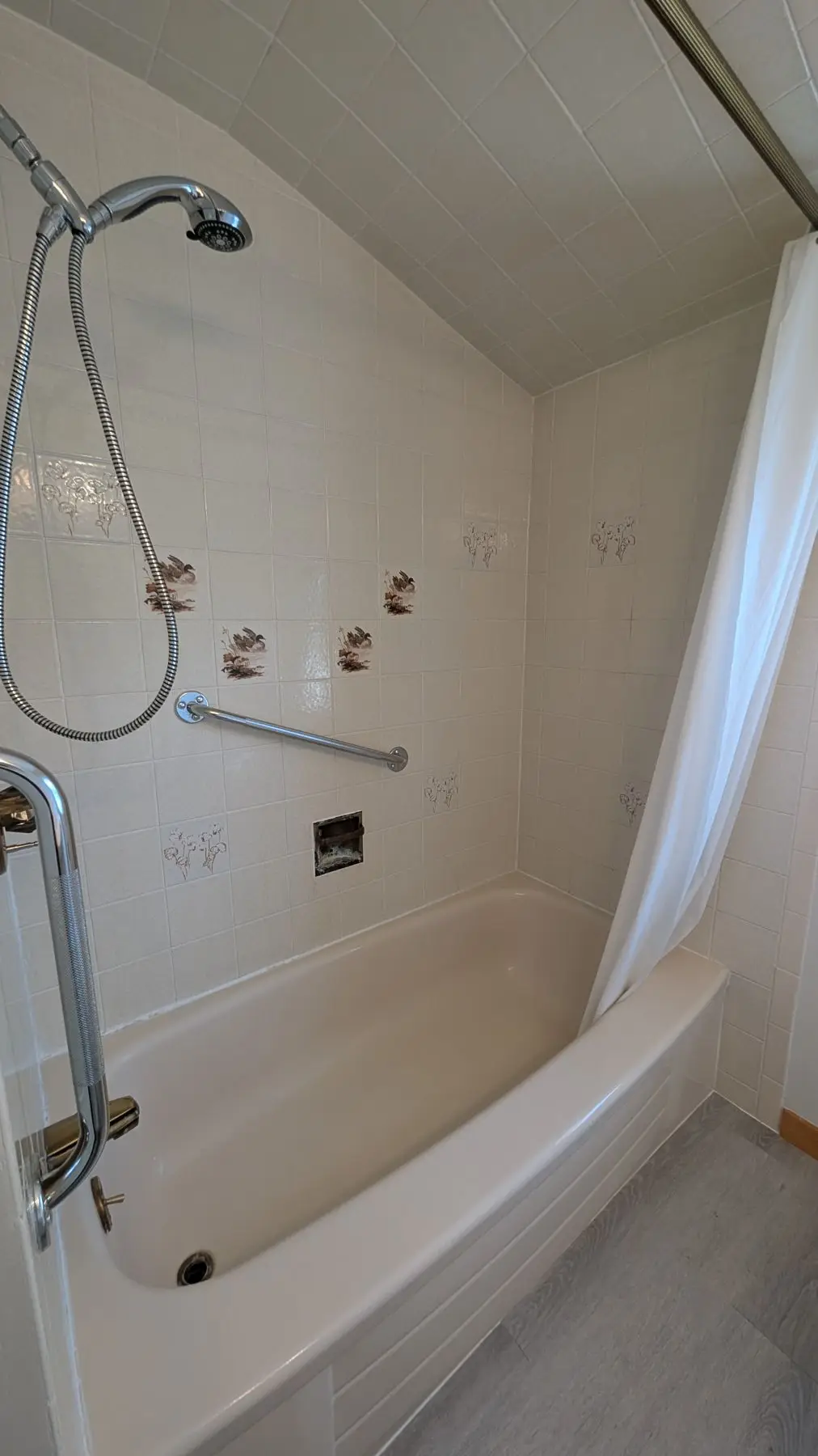 Before — Older bathroom with beige bathtub, tiled walls featuring bird accent tiles, and sloped ceiling.