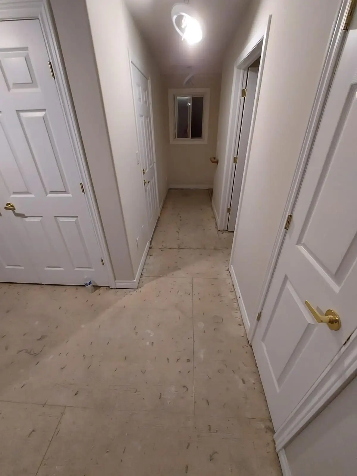 Insulation & drywall — Long narrow hallway view showing subfloor and multiple white paneled doors during interior renovation.