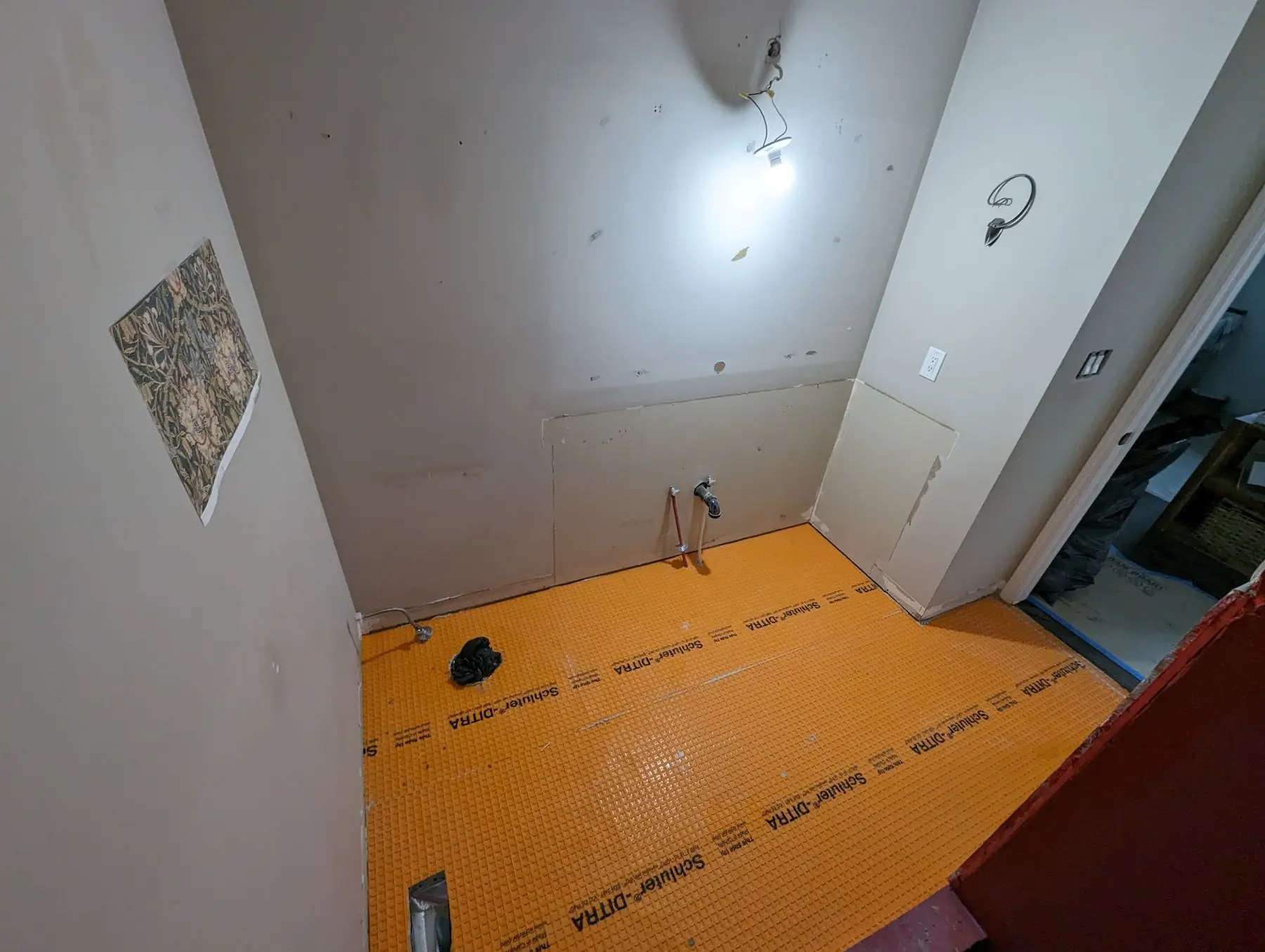 Insulation & drywall — Bathroom during renovation showing orange Schluter-DITRA uncoupling membrane installed on the floor and unfinished drywall.