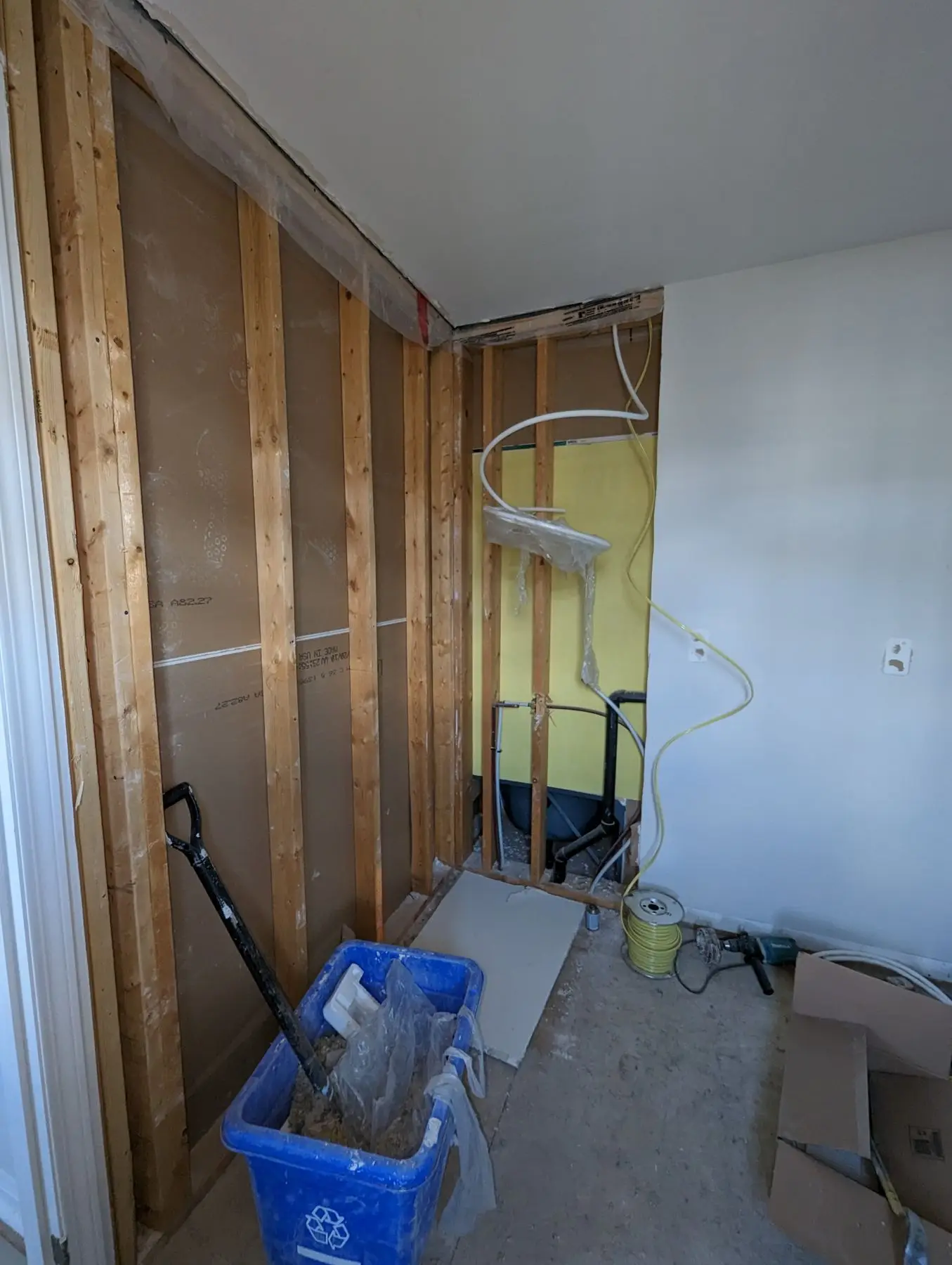 Rough-in — Bathroom during rough-in phase showing exposed wood framing, plumbing pipes, and tools on site.