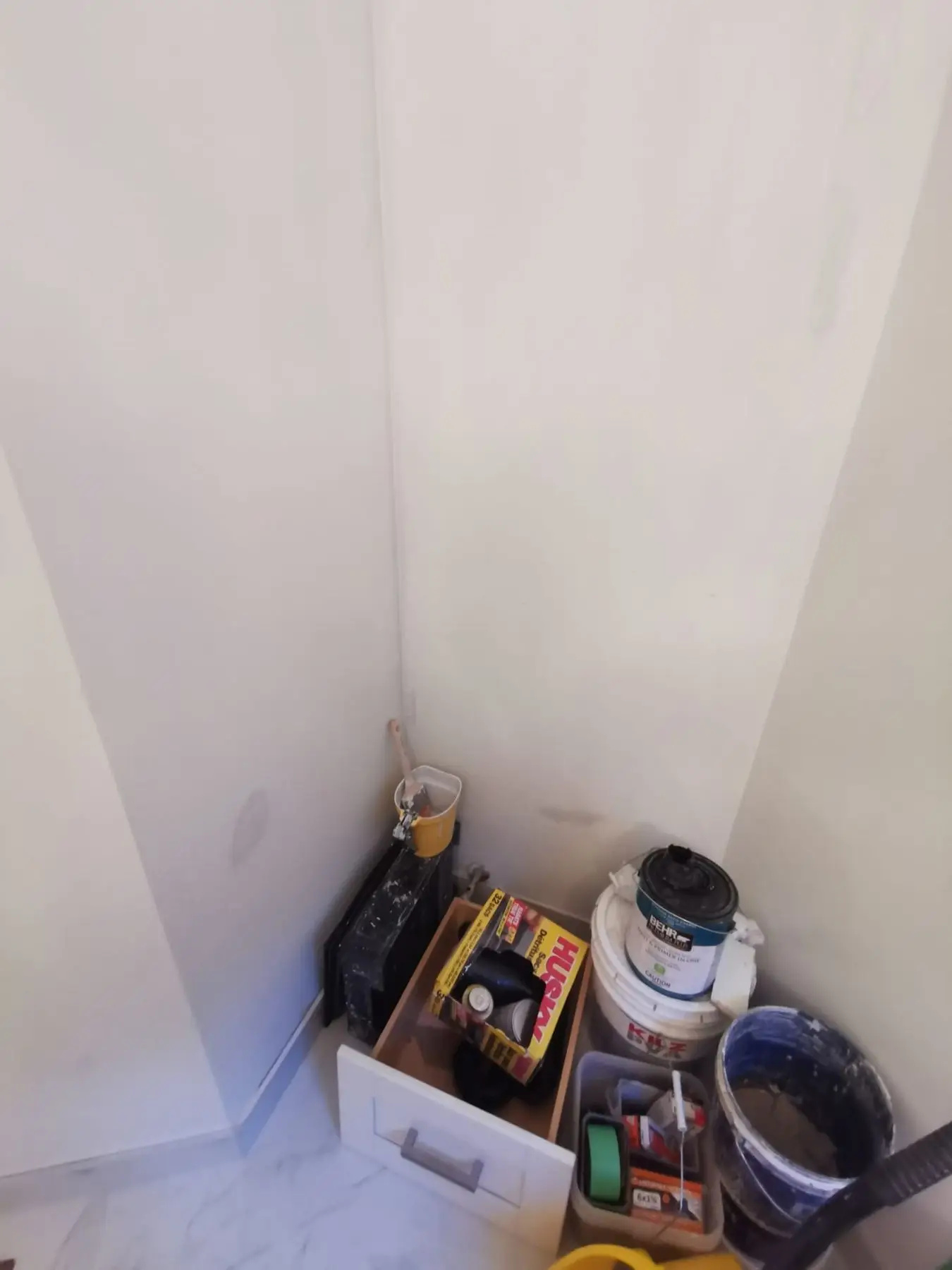 Finishing — Corner of a room with paint buckets, supplies, and tools stored on the floor.