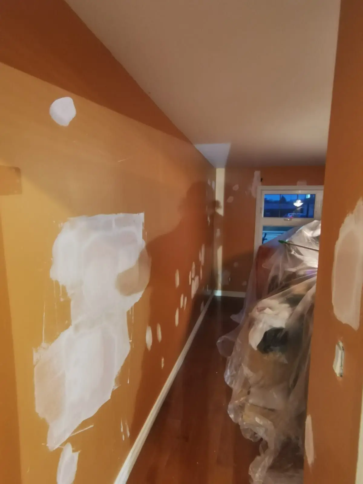 Insulation & drywall — Interior hallway or room with orange walls undergoing drywall patching and repair work.