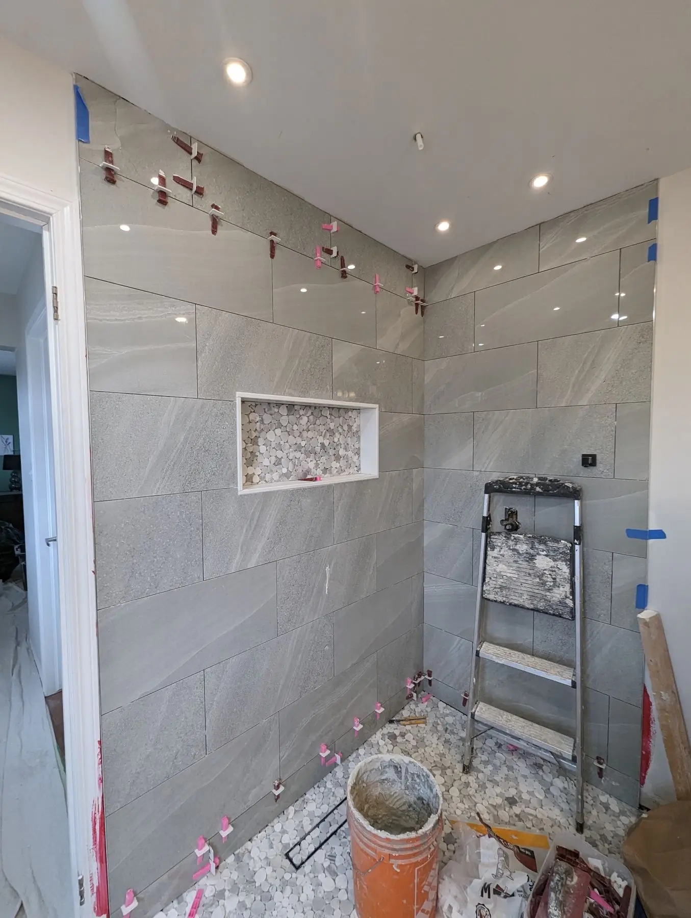 Finishing — Shower enclosure partially tiled with large grey tiles and tile leveling system, featuring a niche and pebble floor.