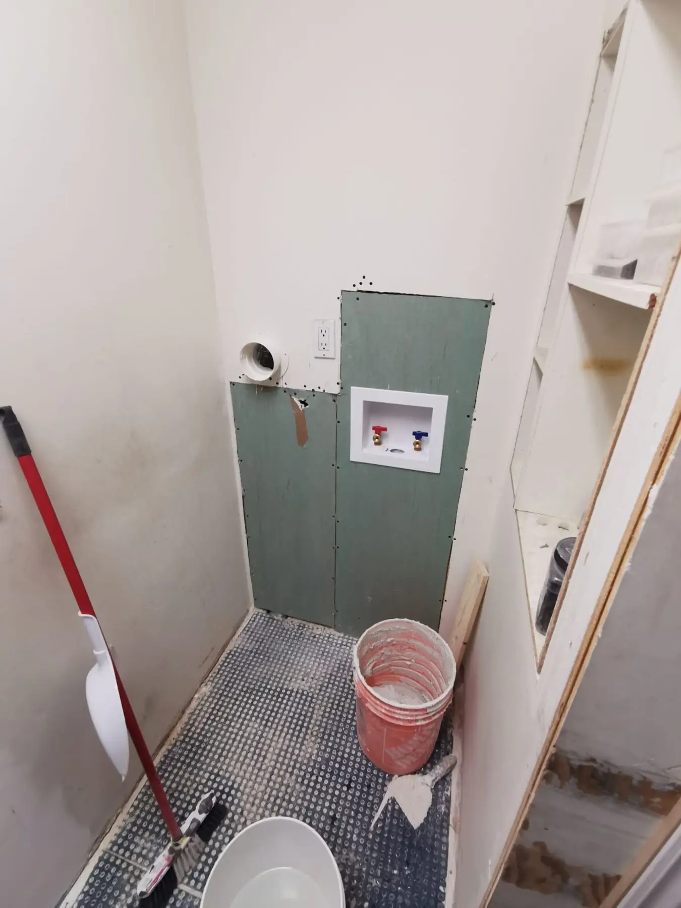 Insulation & drywall — Laundry room during drywall repair showing water supply box, vent, and tools on floor.