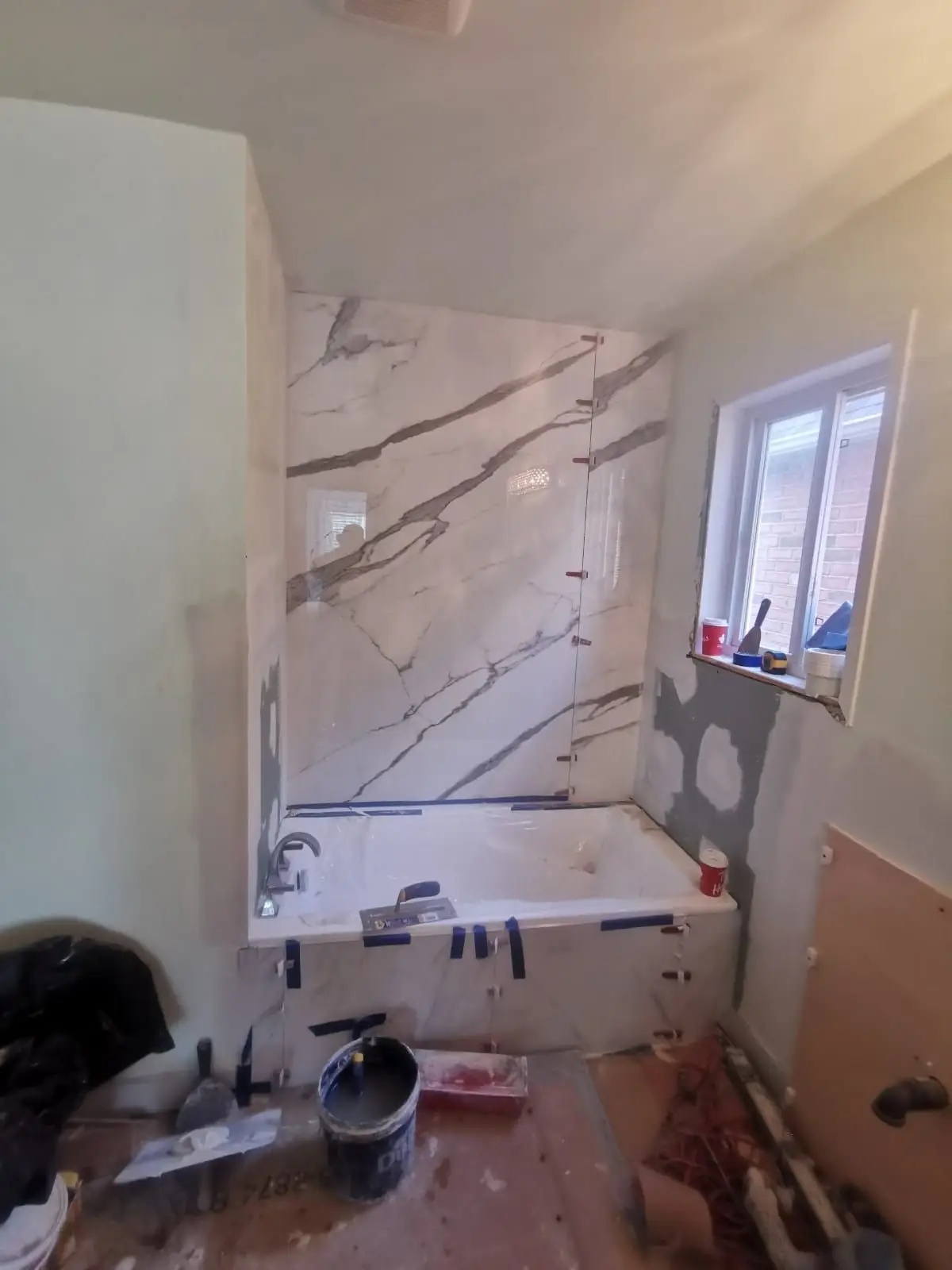 Finishing — Bathroom renovation showing large format marble-look tile installation around bathtub and unpainted drywall.