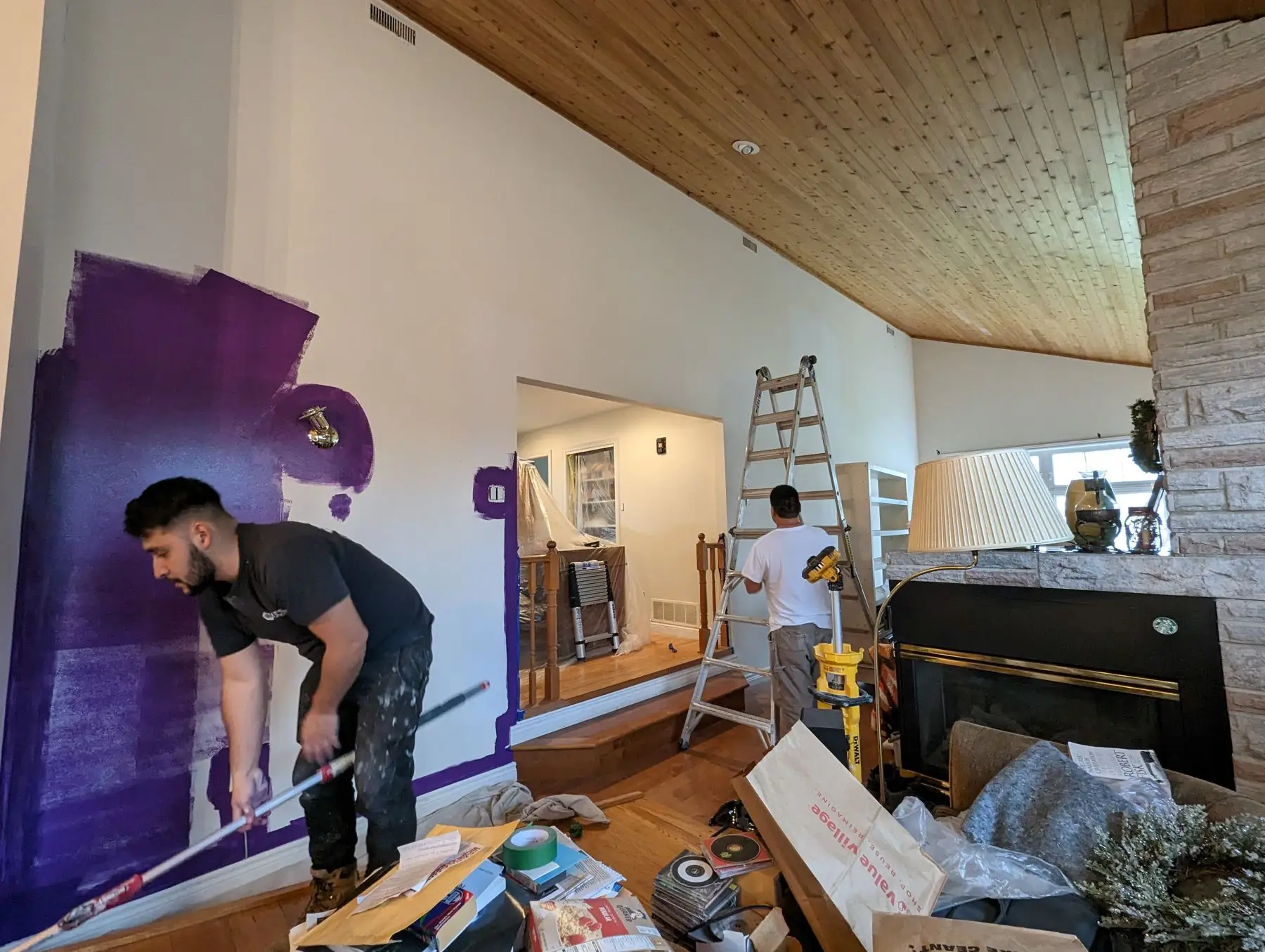 Finishing — Workers painting the wall purple in a vaulted living room with a stone fireplace.