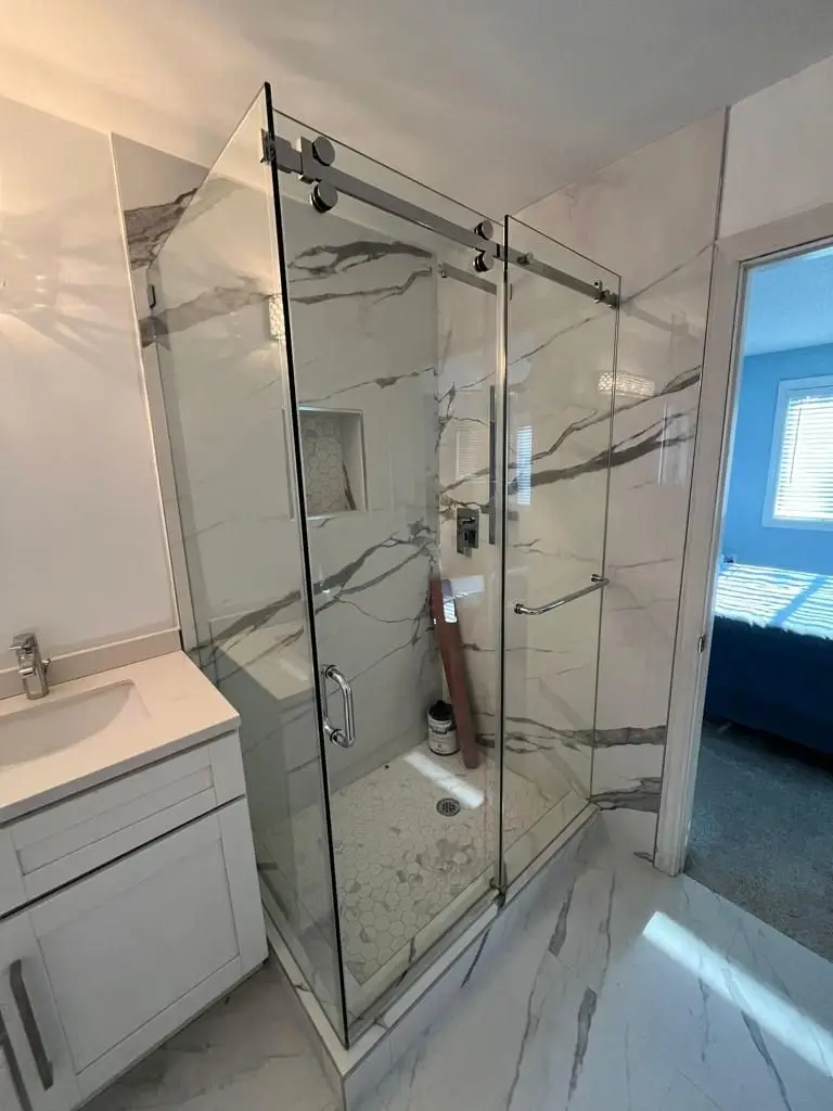 Finishing — Bathroom with completed marble-look tile shower, sliding glass door, white vanity, and construction debris left inside.