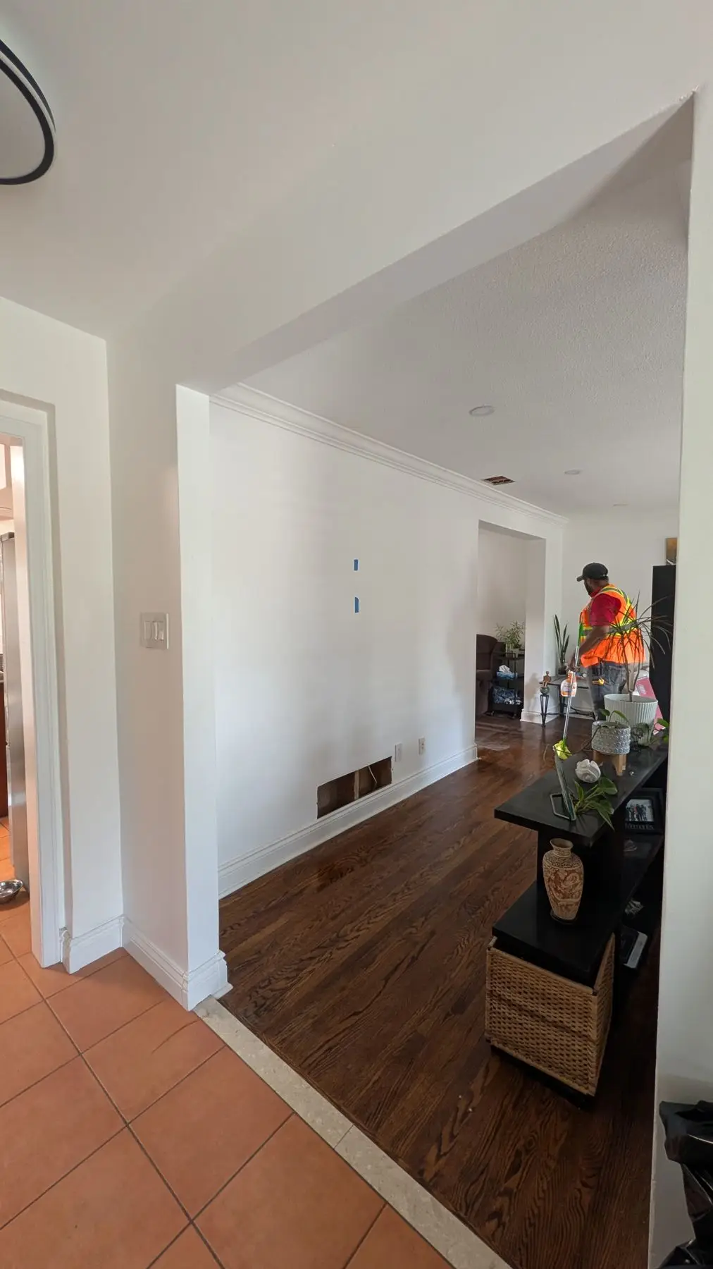 Finishing — Worker in high-vis vest stands in a living space with hardwood flooring near an open archway.