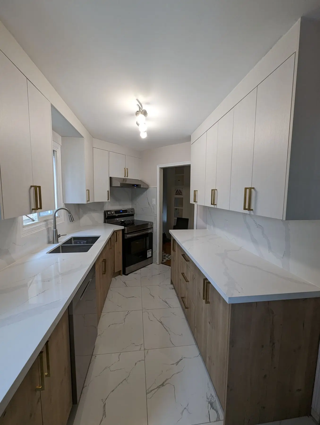 Finished — A fully renovated galley kitchen featuring white quartz countertops, two-tone wood and white cabinets, and marble-look floor tiles.