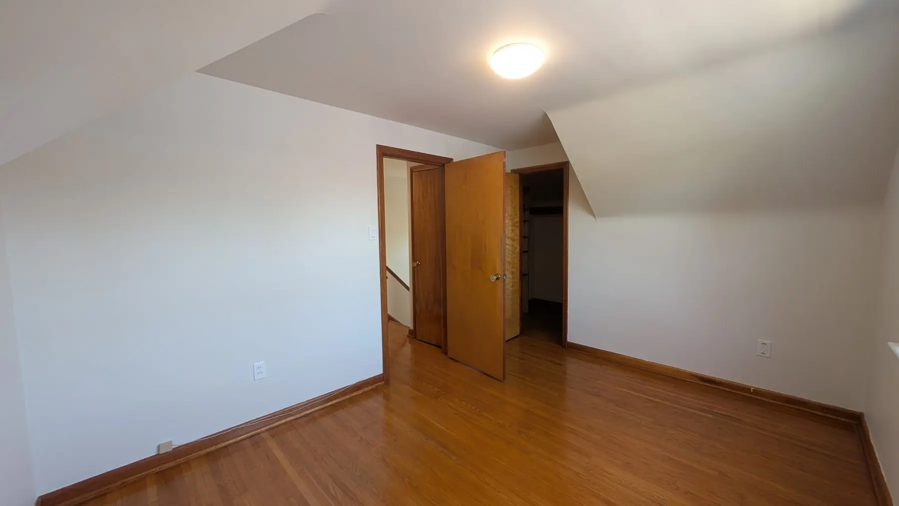 Finished — Finished bedroom with hardwood floors, white walls, sloped ceiling, and wooden doors.