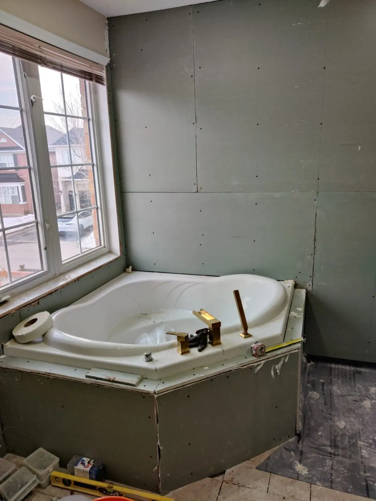 Insulation & drywall — Corner soaker tub with gold faucet installed amid greenboard drywall installation in a bathroom.