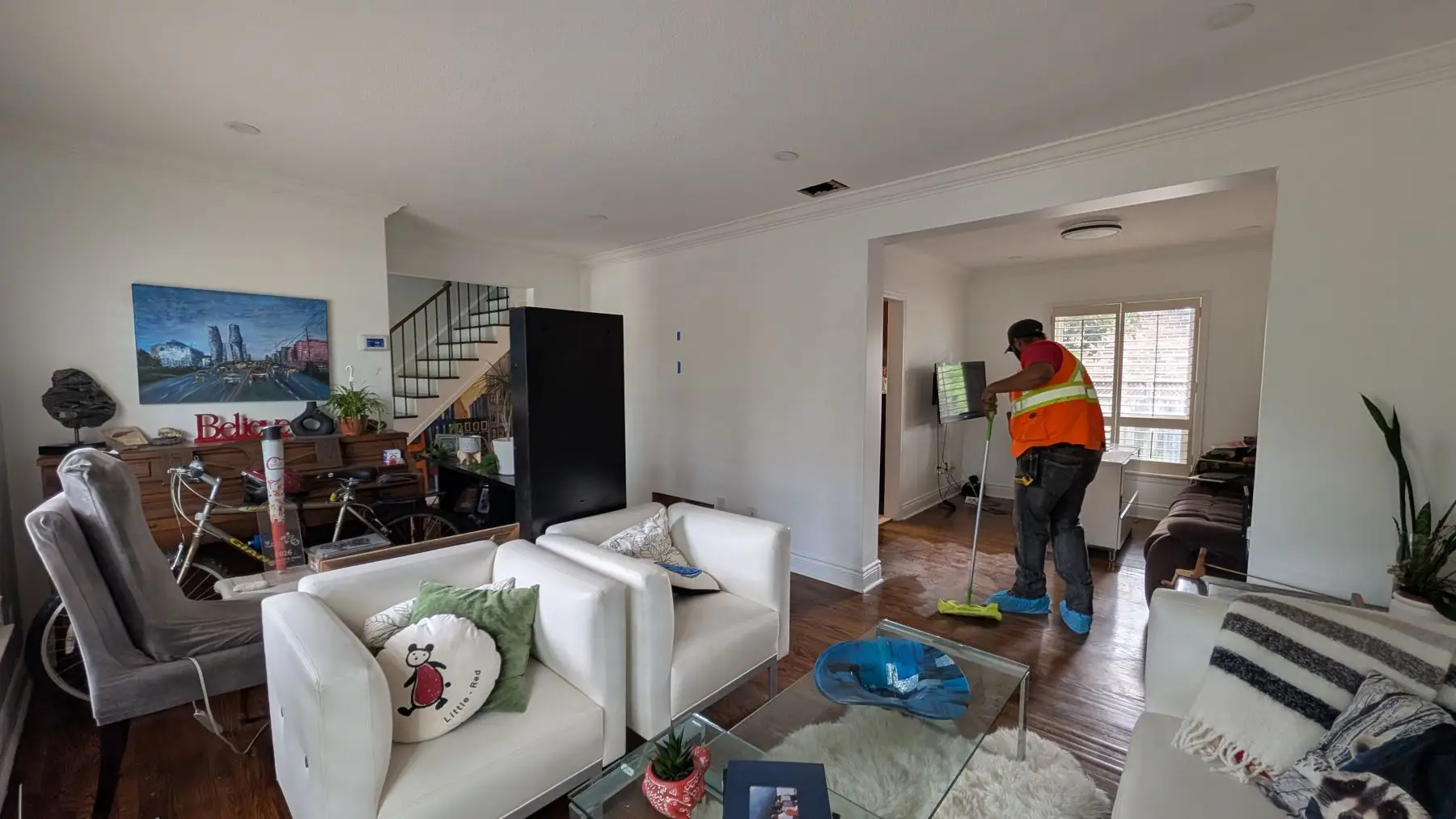 Finishing — Worker in high-vis vest and booties cleaning living space floor with a mop.