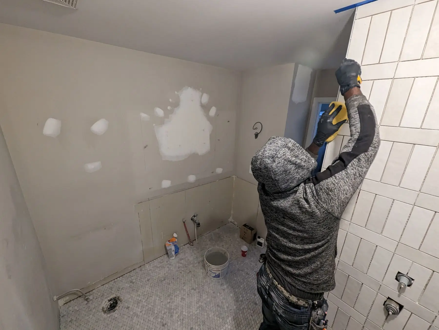 Finishing — Worker grouting or cleaning vertical stacked white tiles in a bathroom shower area.