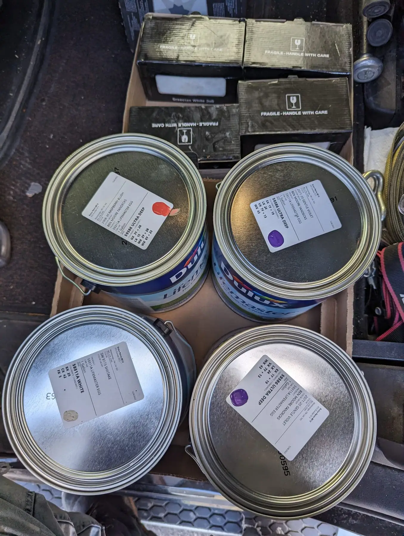 Finishing — Overhead view of four paint cans and boxes inside a vehicle cargo area.