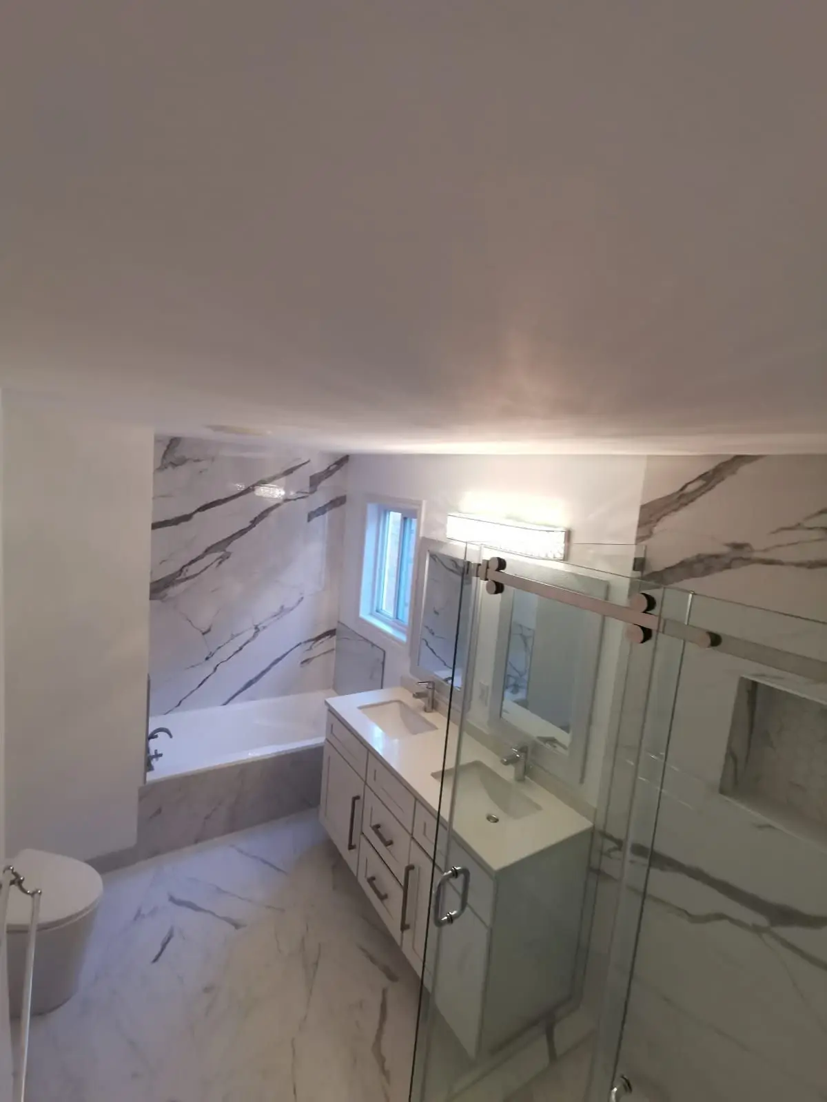 Finished — High angle shot of a finished modern bathroom with double vanity, glass shower, and marble-look tiling.