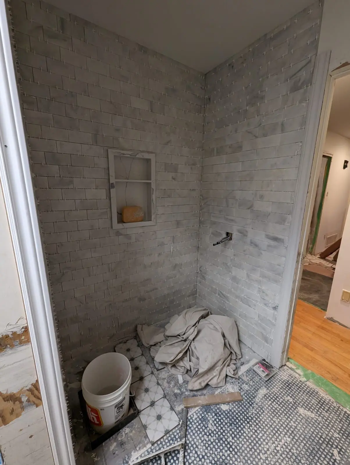 Finishing — Bathroom shower walls tiled with gray subway tile and a built-in niche, featuring tile spacers.