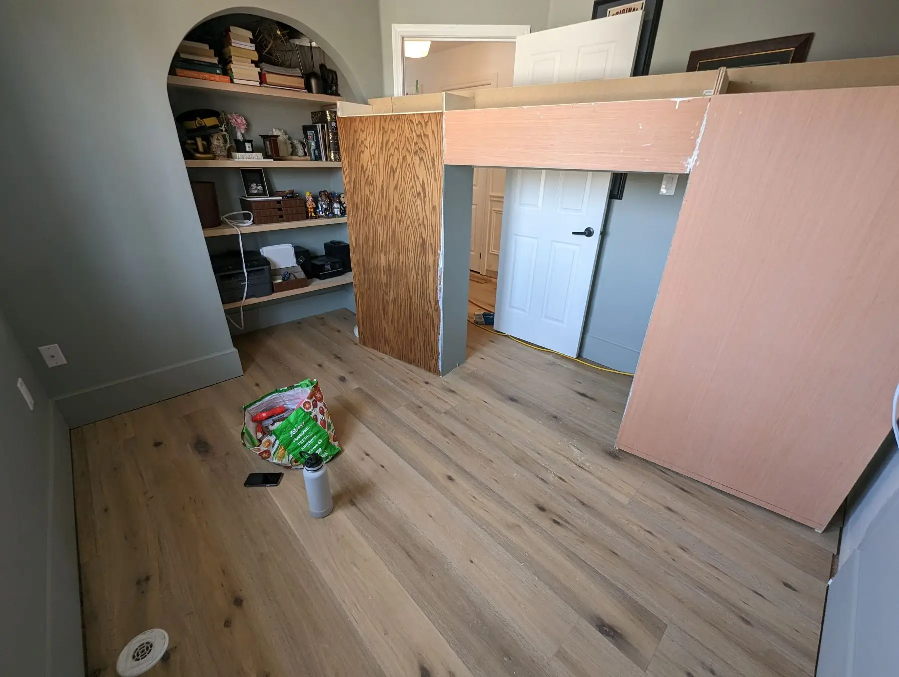 Finishing — Bedroom under construction showing custom built-in bed framing and arched shelving alcove with unfinished wood surfaces.
