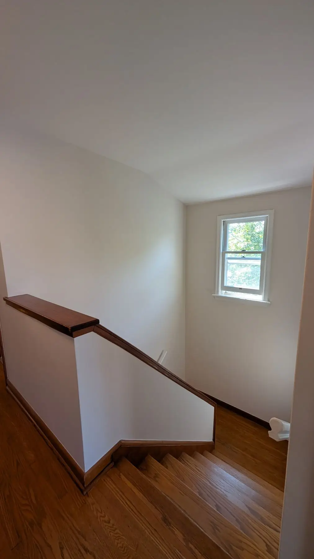 Finished — Finished wooden staircase with white half-wall railing and window looking down the stairwell.